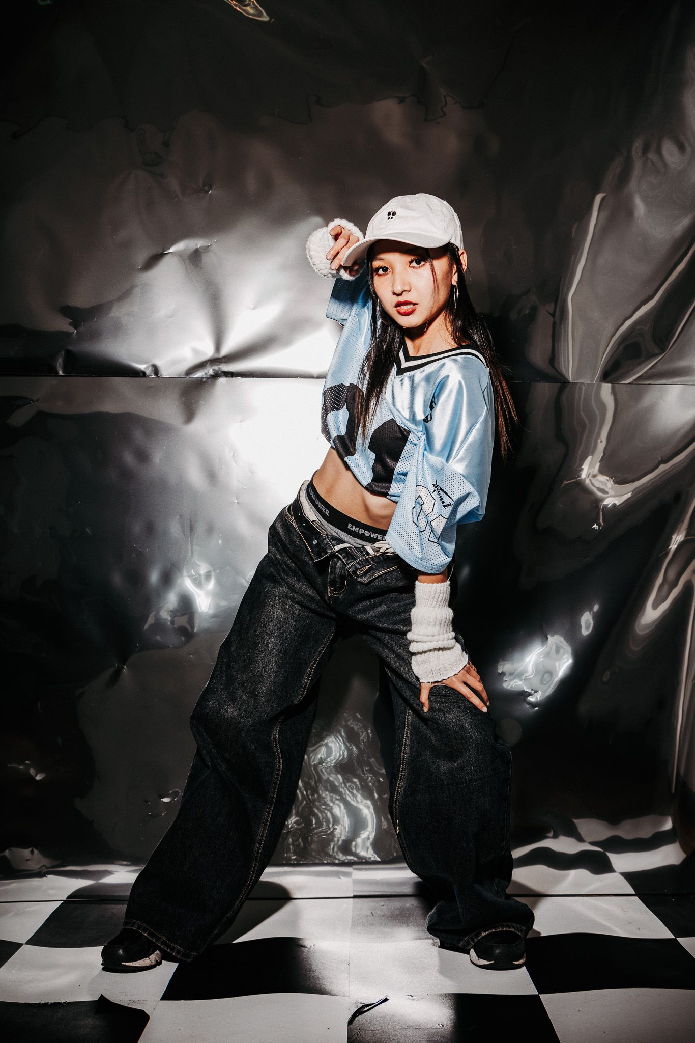 Artistic fashion portrait with baggy pants and light blue top in dramatic lighting against dark backdrop.