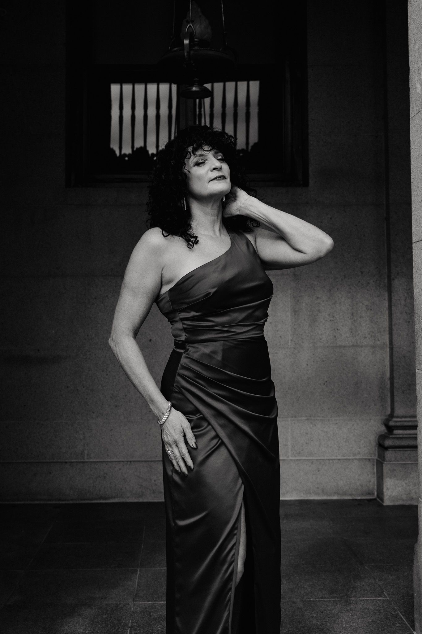 A person in a sleek black satin dress poses expressively in a dramatic black and white portrait series.