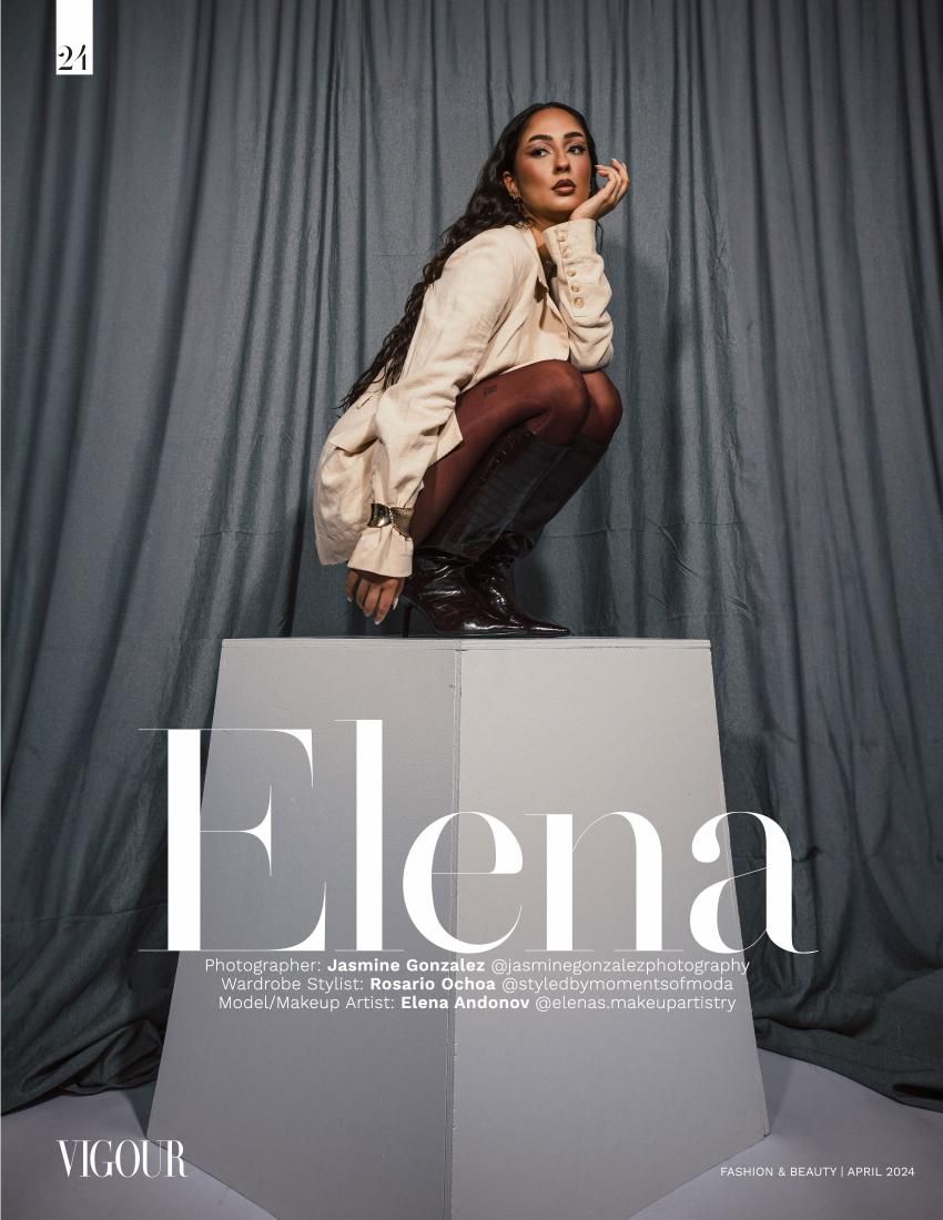 Editorial fashion photo of model crouching on cube pedestal against gray curtain backdrop.