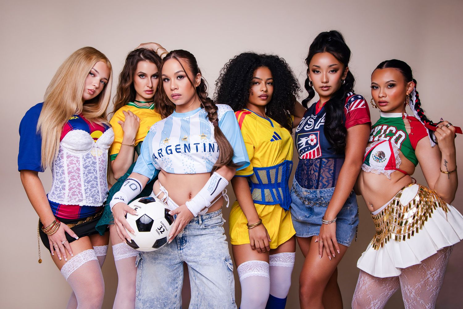 Seven women in colorful international soccer jerseys pose together, one holding a soccer ball, in a World Cup themed photo shoot.