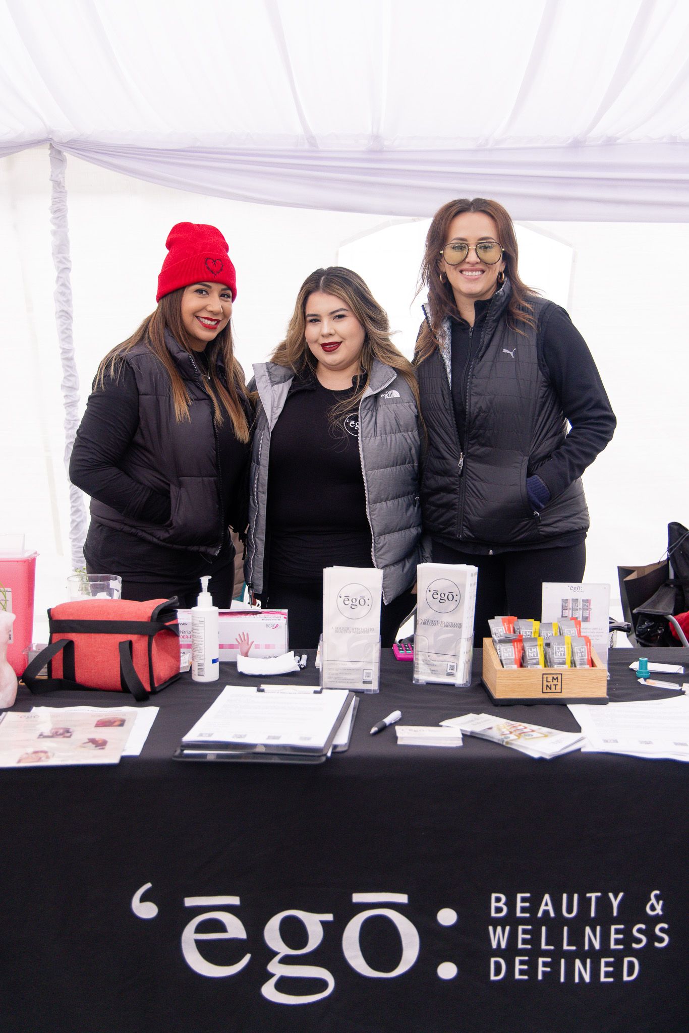A black vendor booth display with red accents showing beauty and wellness products under a white tent.