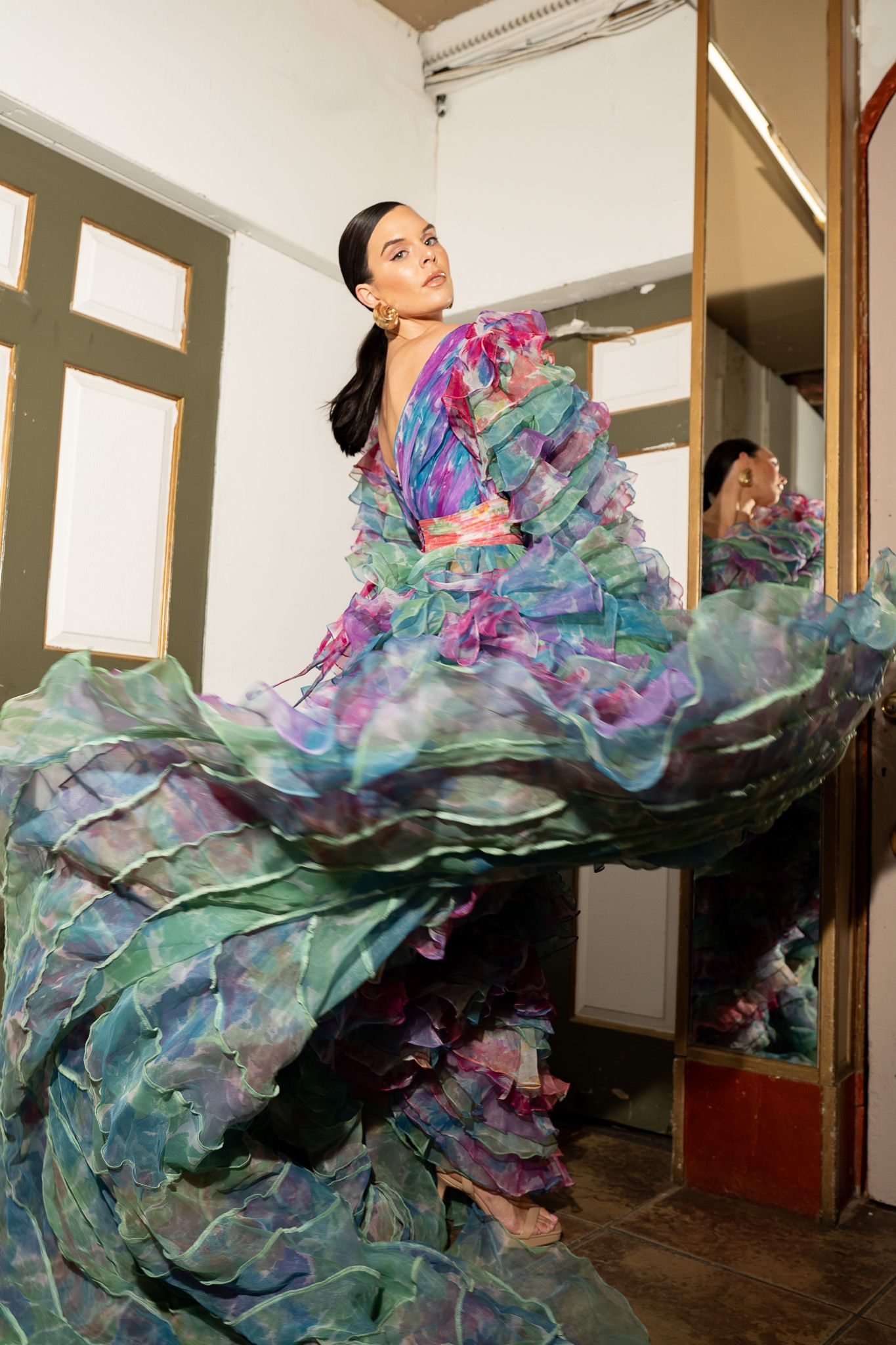 A flowing multicolored dress with turquoise and purple hues captured in dynamic motion against a white interior space.