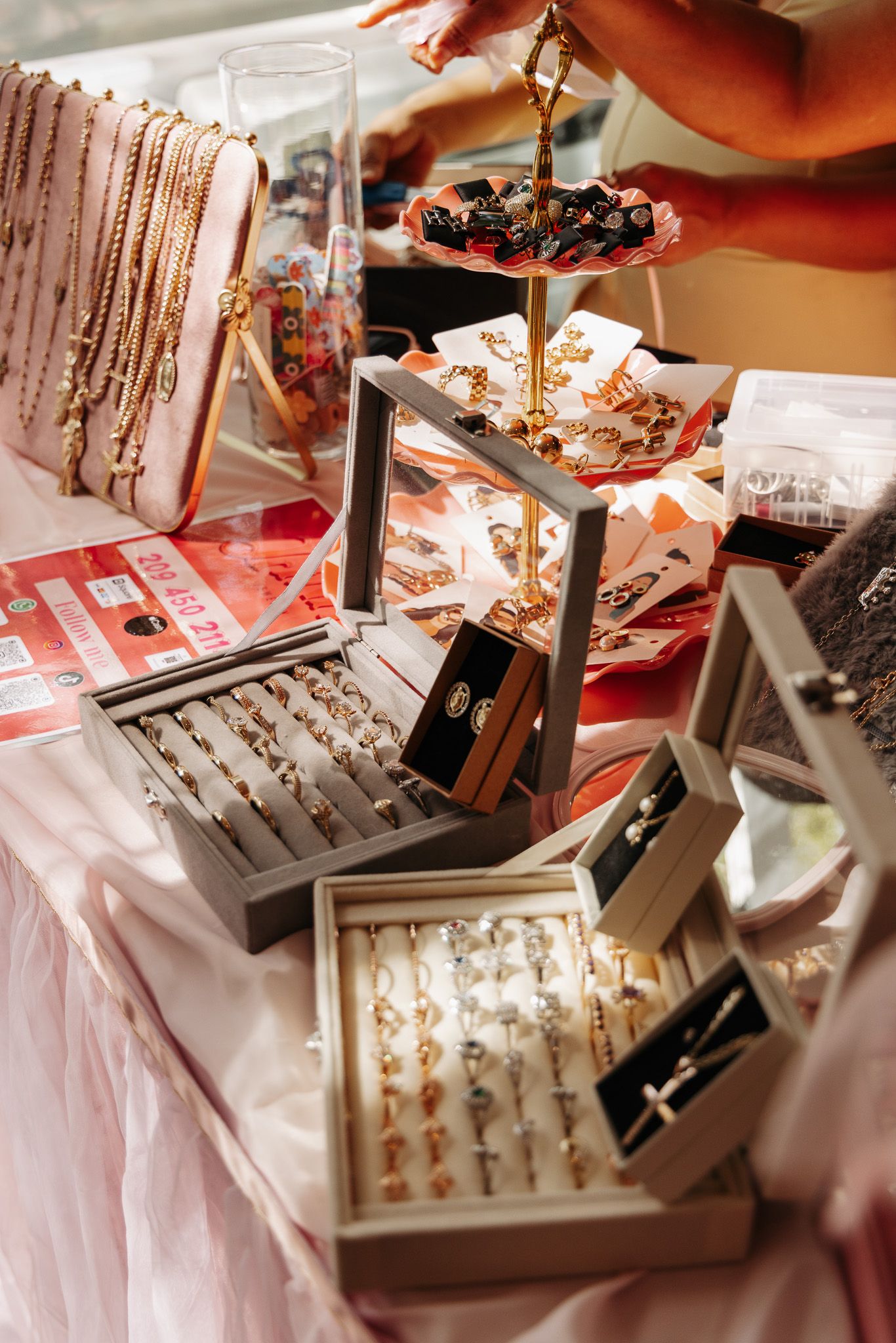 Jewelry display boxes and trays with rings and accessories arranged on pink fabric at a retail showcase.
