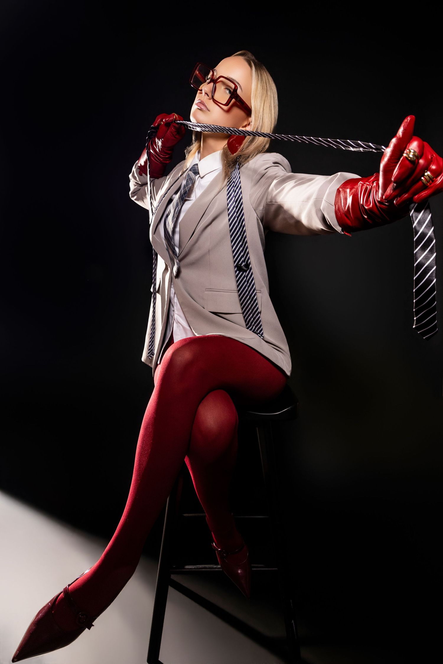 Fashion model poses in red pants and white blazer against dark background with dramatic lighting and shadows.