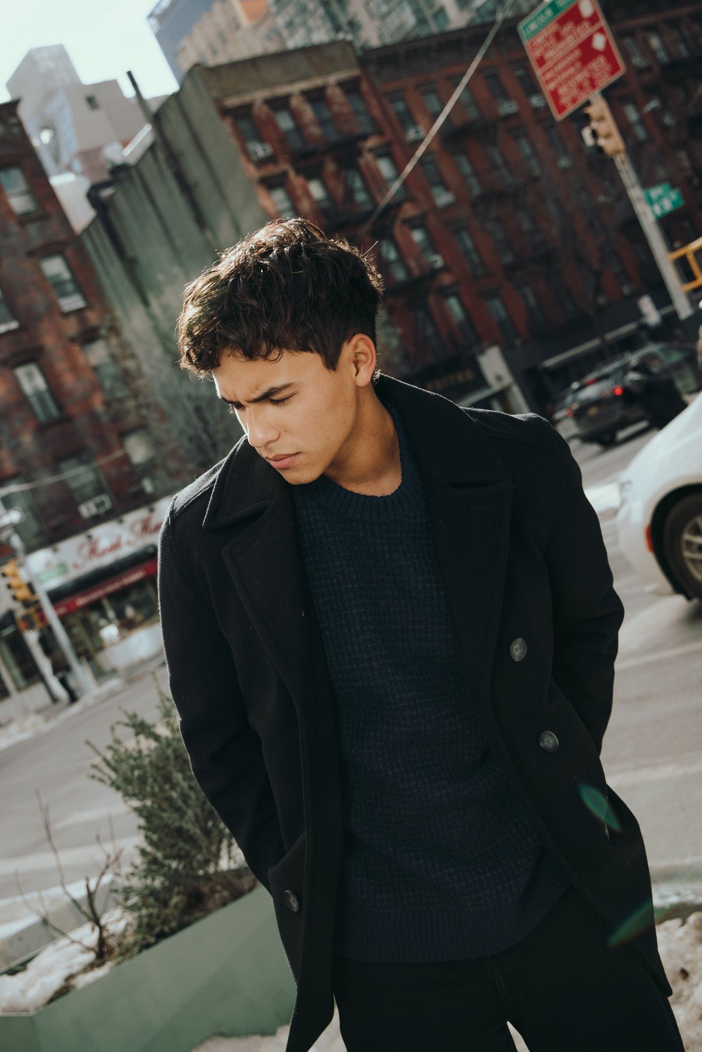Person in black winter coat and sweater standing on city street with brick buildings in background during daytime.