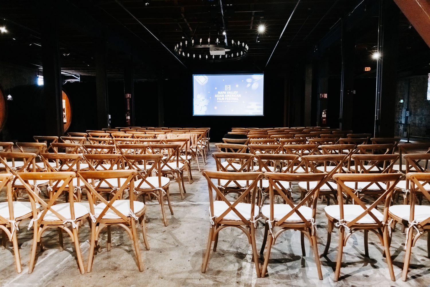 Wooden cross-back chairs arranged in rows at an indoor venue with string lights overhead.