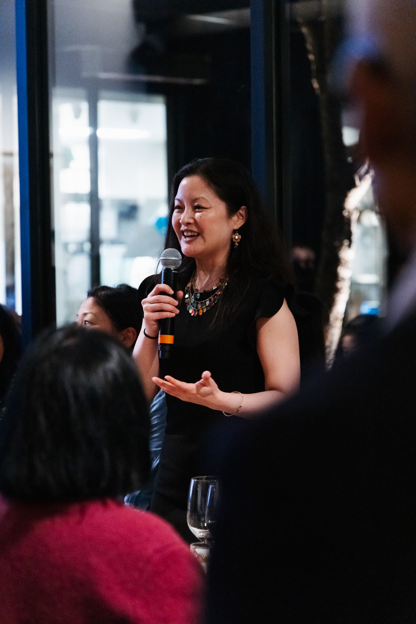 A speaker addresses an audience at an indoor event while holding a microphone and gesturing enthusiastically.