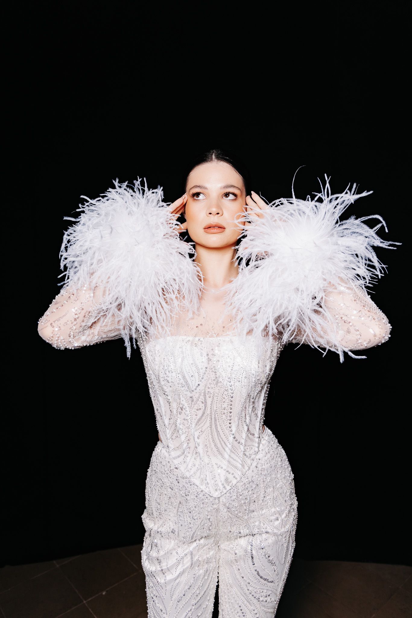 Dramatic white feathered ensemble with crystal embellishments against black backdrop.