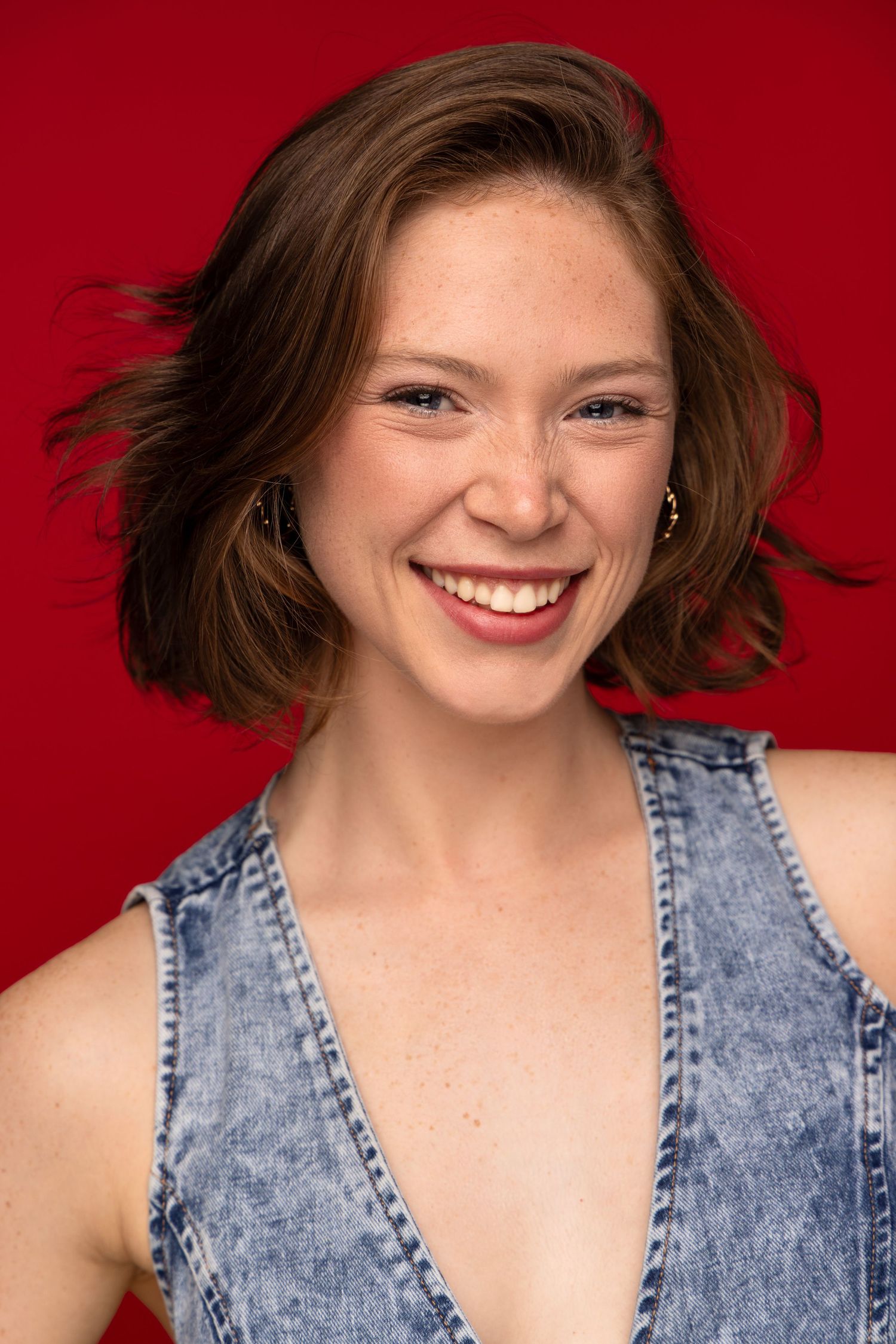 Professional headshot series against a red background featuring a joyful expression and denim top.