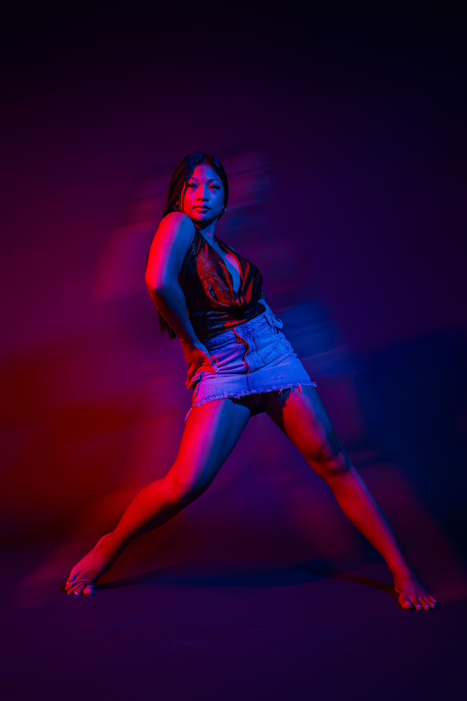 Contemporary dancer in denim strikes dramatic pose against neon-lit background.