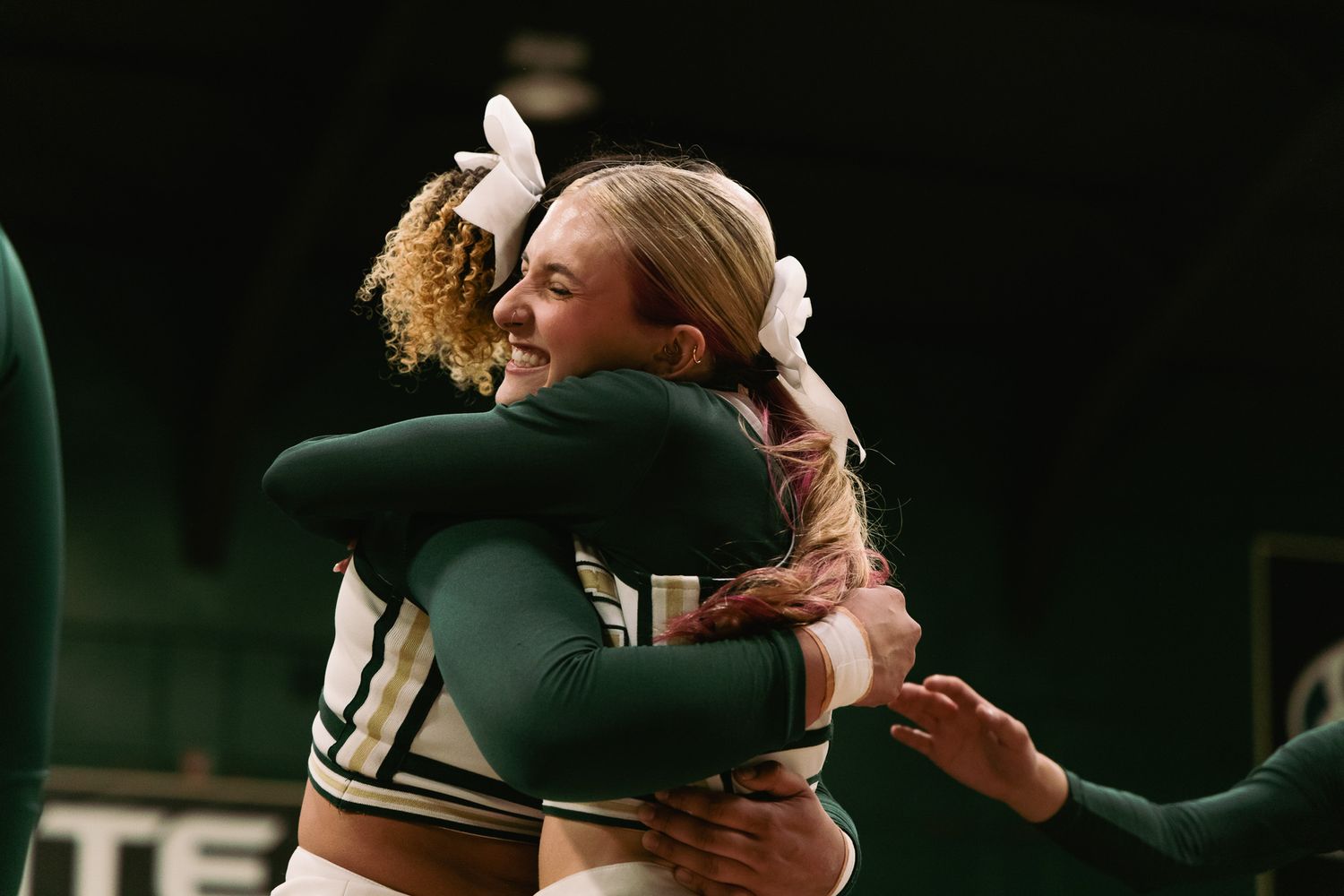 Two cheerleaders in green uniforms share a warm hug on the court during a cheerleading event.