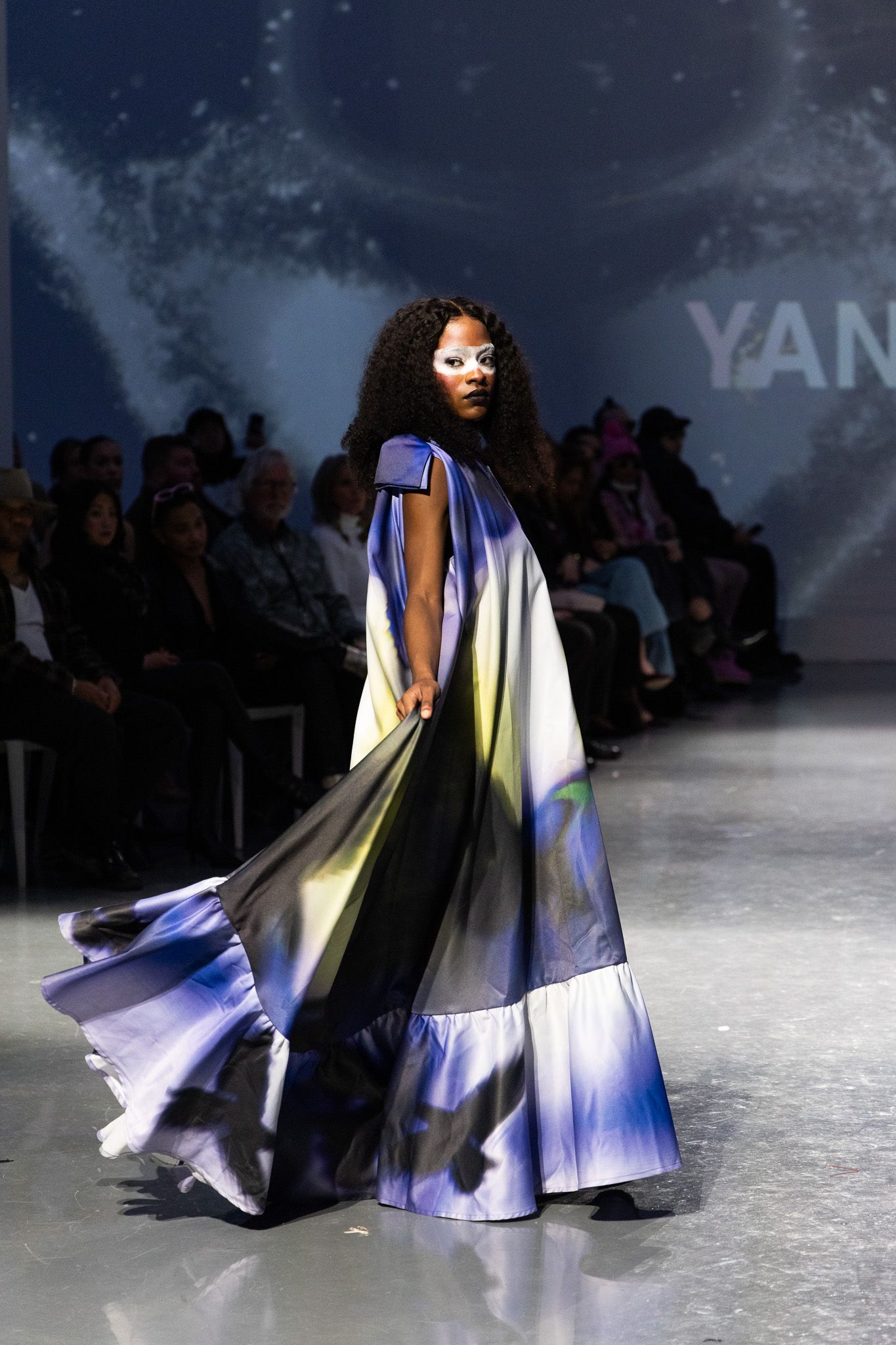 Dramatic flowing blue and white gown sweeping across runway with silhouetted audience in background.