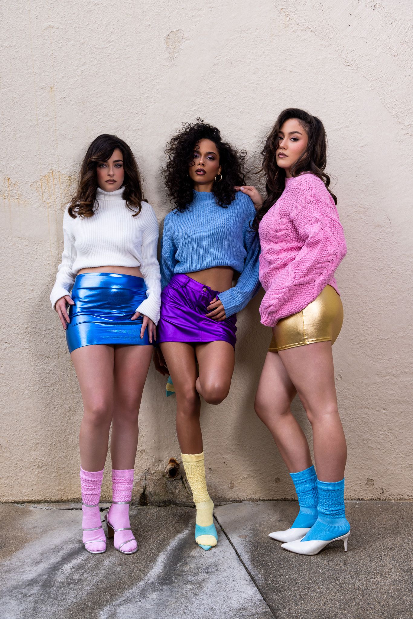 Three people in retro-style athletic shorts and knee socks pose playfully against a wall in matching poses.