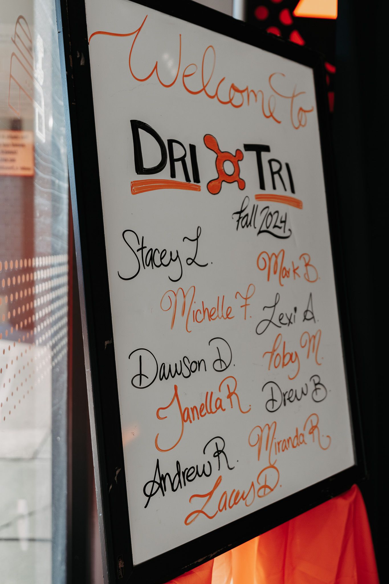 Names written in black and orange marker on white paper displayed in dark frames against a wall.