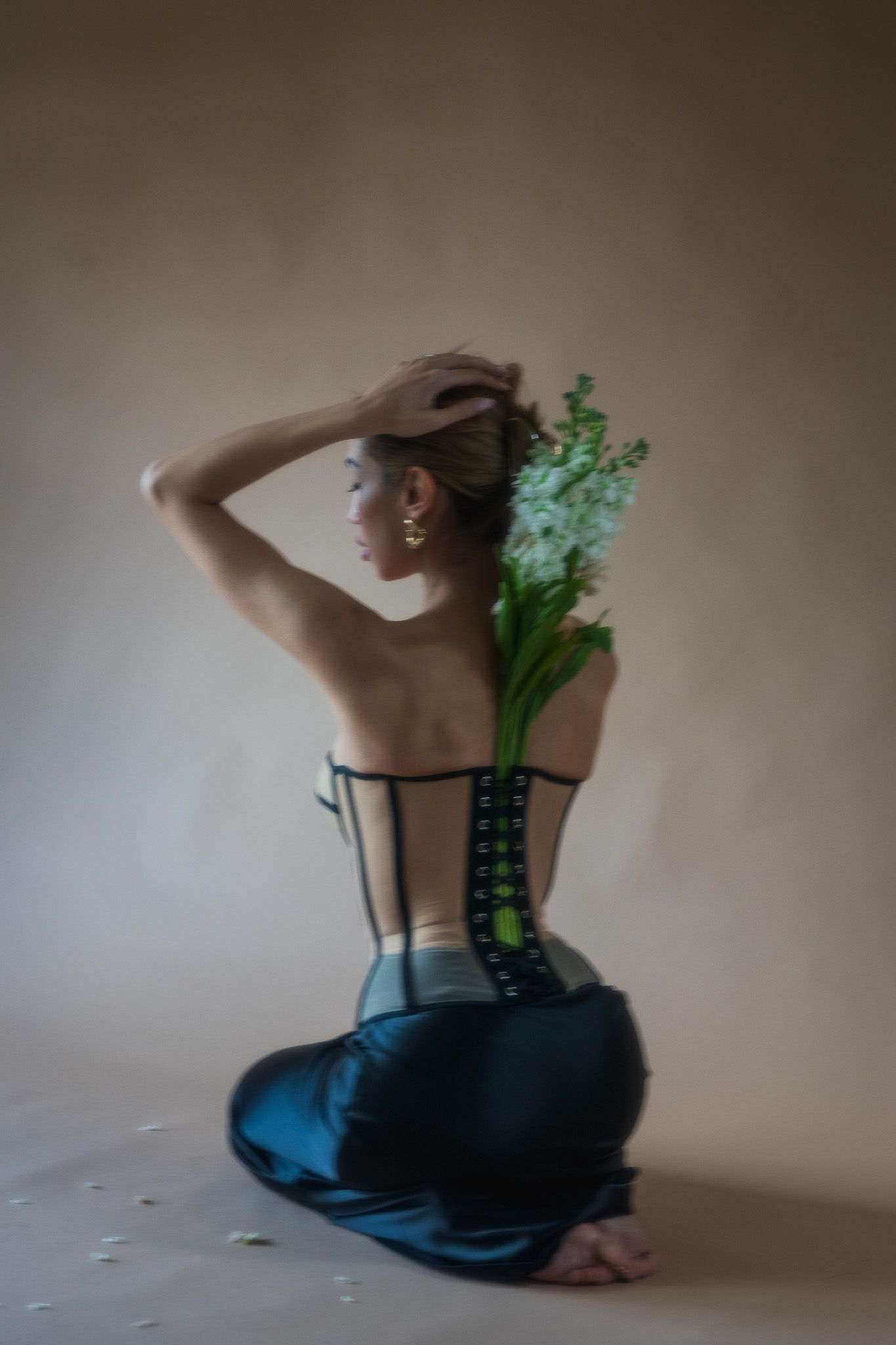 Artistic back view portrait in moody lighting features teal dress and vibrant green floral arrangement.