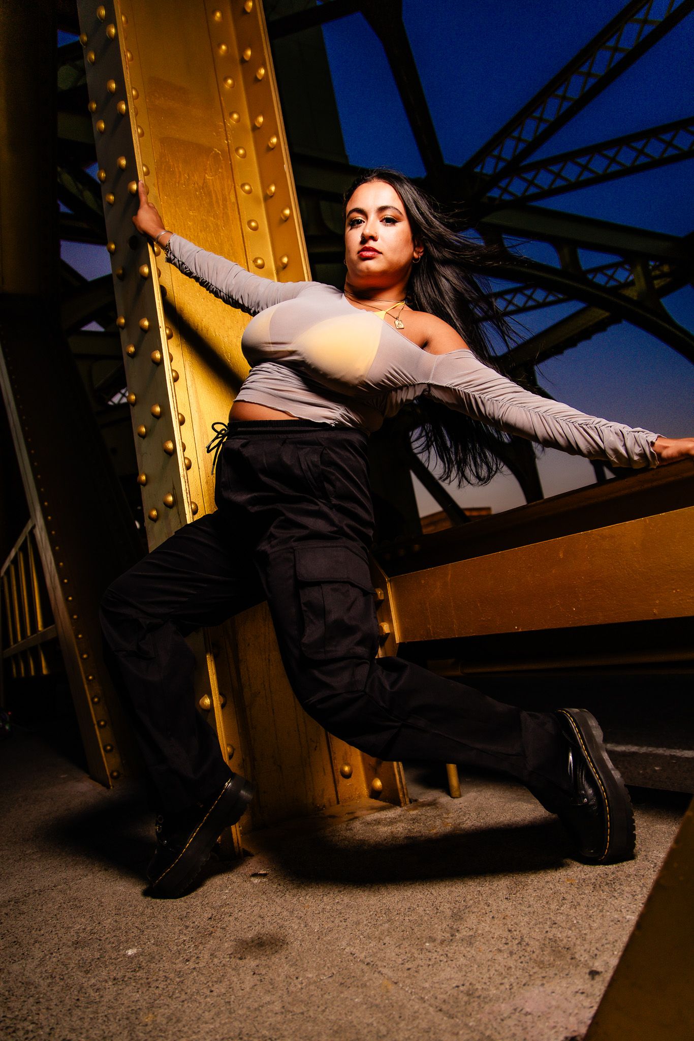 A series of dramatic portrait shots at dusk against an industrial bridge structure with warm golden lighting.