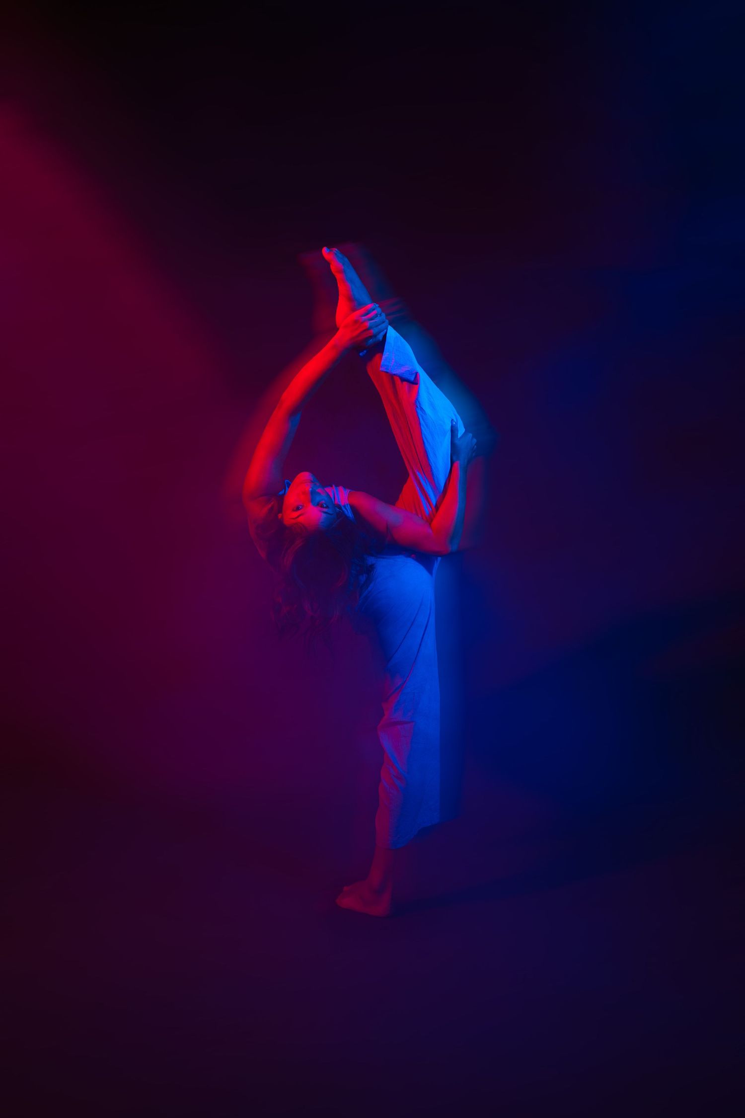 Dancer in dramatic pose illuminated by red and blue lighting creating an ethereal silhouette effect.