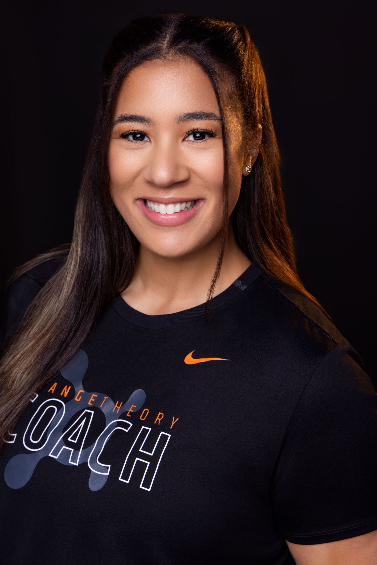 Professional headshot of someone wearing a black Nike t-shirt with 'Coach' text against a dark background.