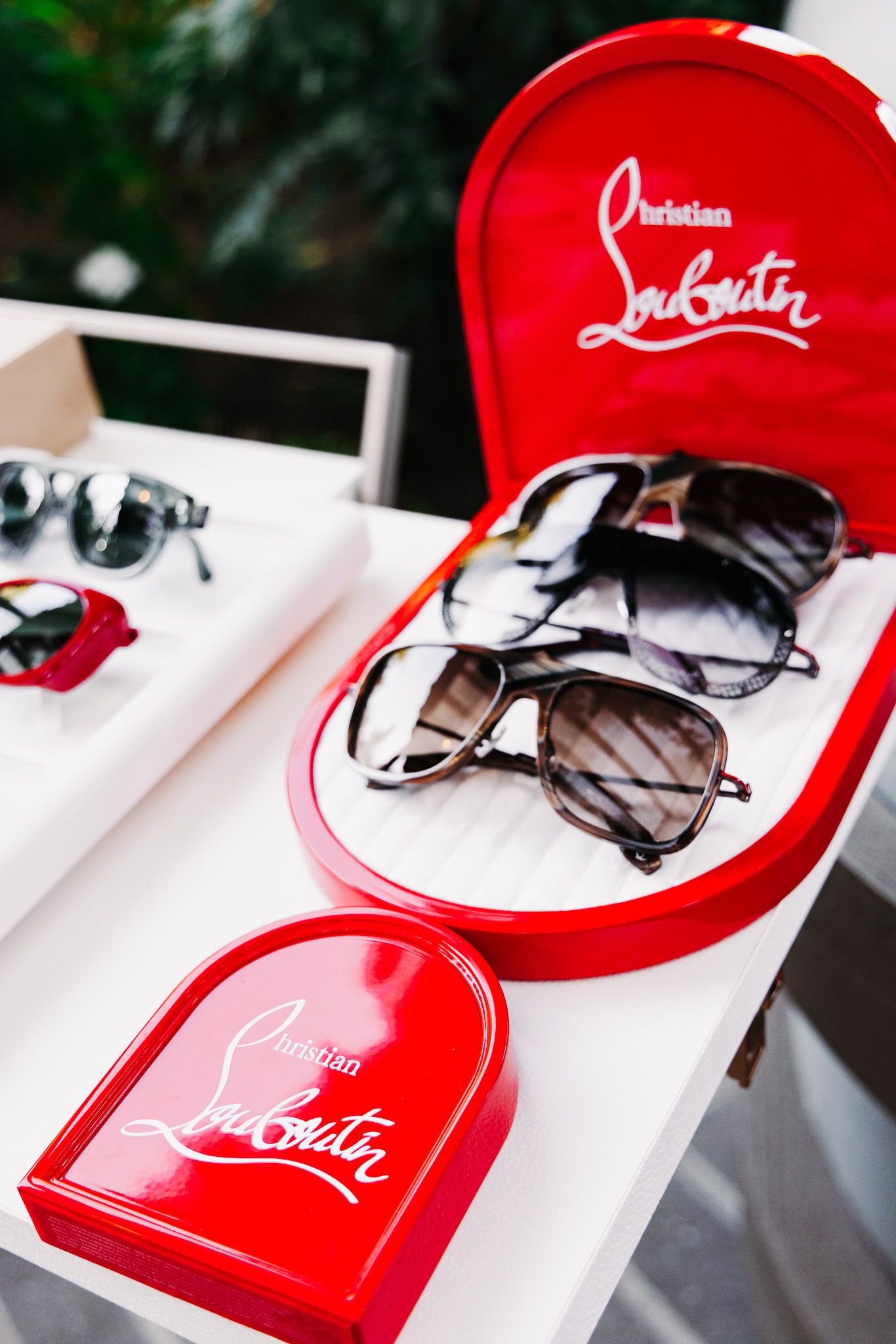 A collection of red Christian Louboutin branded baseball caps and sunglasses displayed on a white surface.