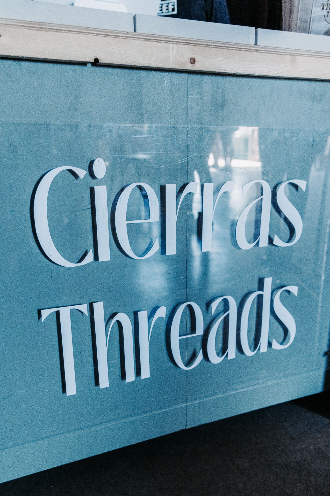 Light blue sign with white raised letters reading Cierras Threads, a clothing boutique storefront display.