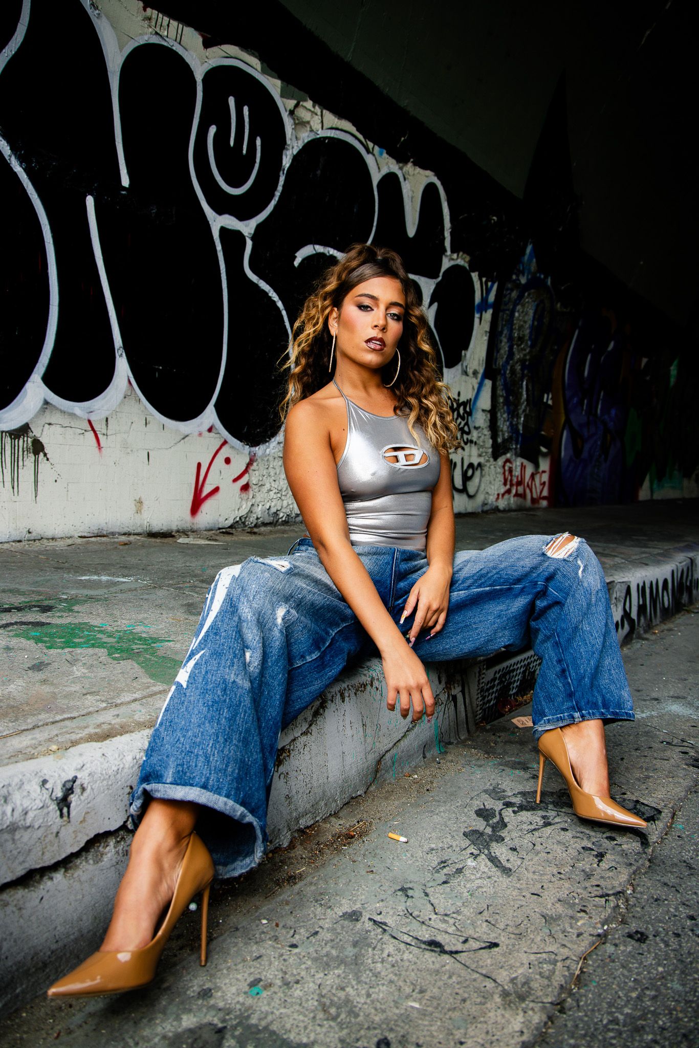 Fashion model in denim and heels poses dramatically against graffiti wall in urban photoshoot series.