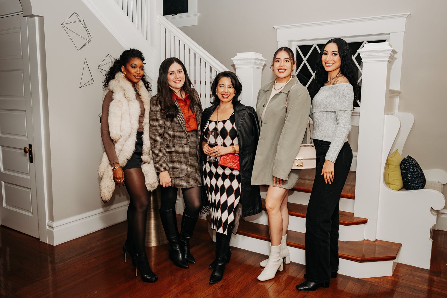 Group of women in stylish outfits standing together near a white staircase.