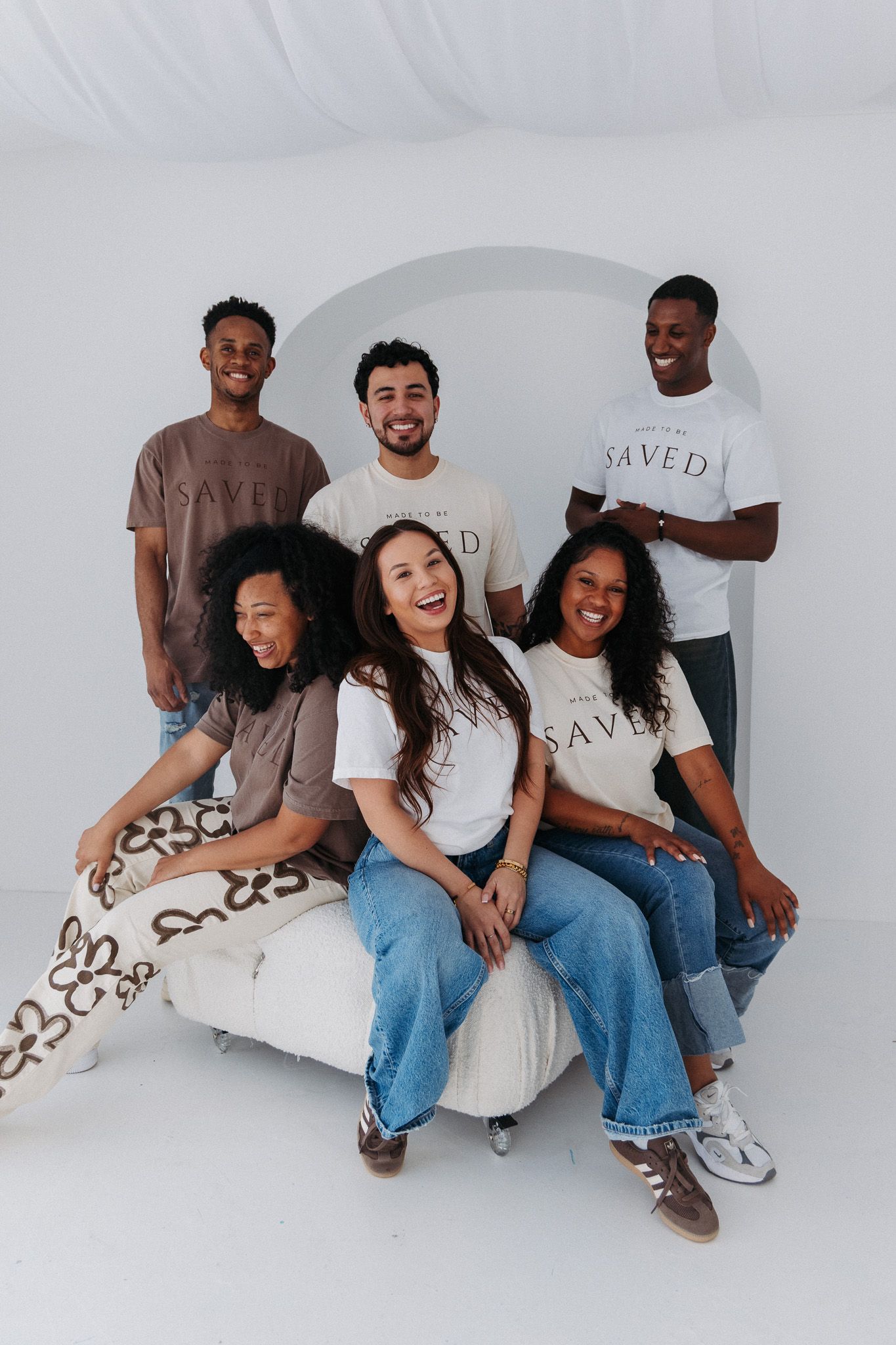 Group of diverse friends wearing matching branded t-shirts pose together in white studio setting.