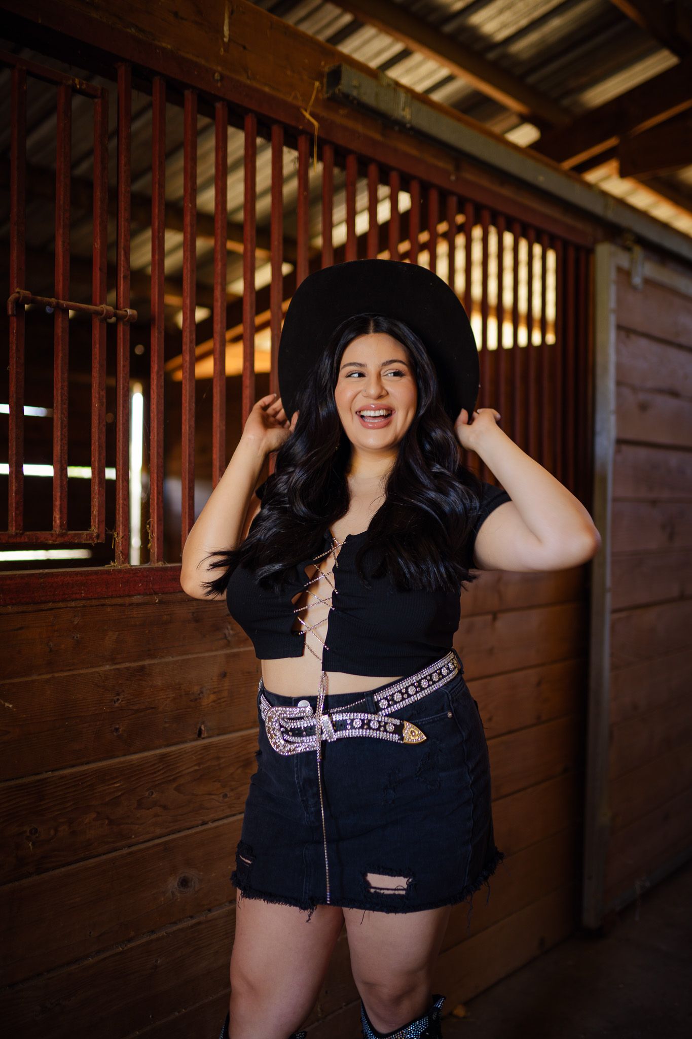 A photoshoot in a rustic barn stable with dark wooden stalls and slats creating a moody lighting atmosphere.