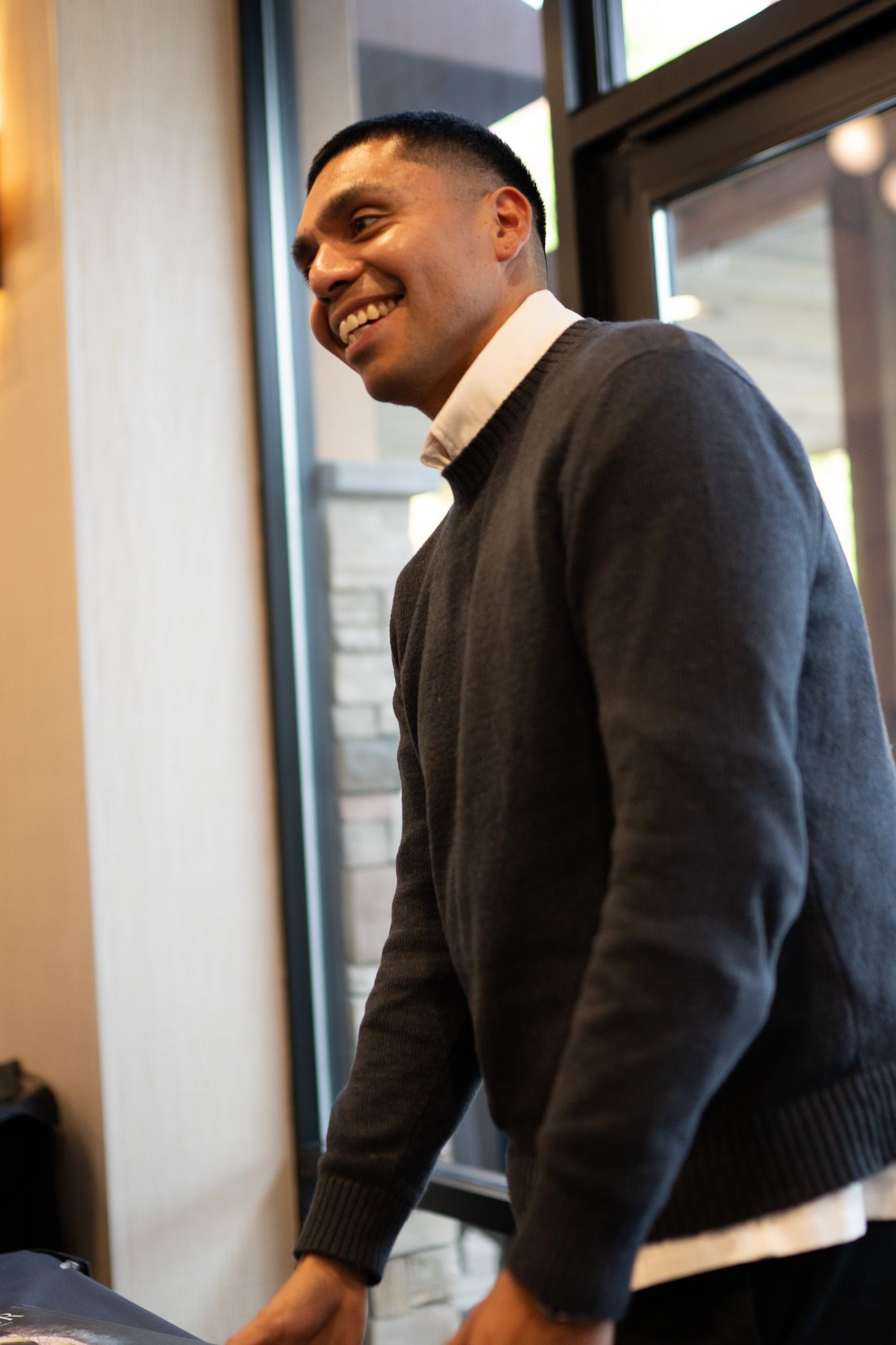 A person in a dark sweater shown in multiple angles sitting and smiling in an office setting with windows in the background.