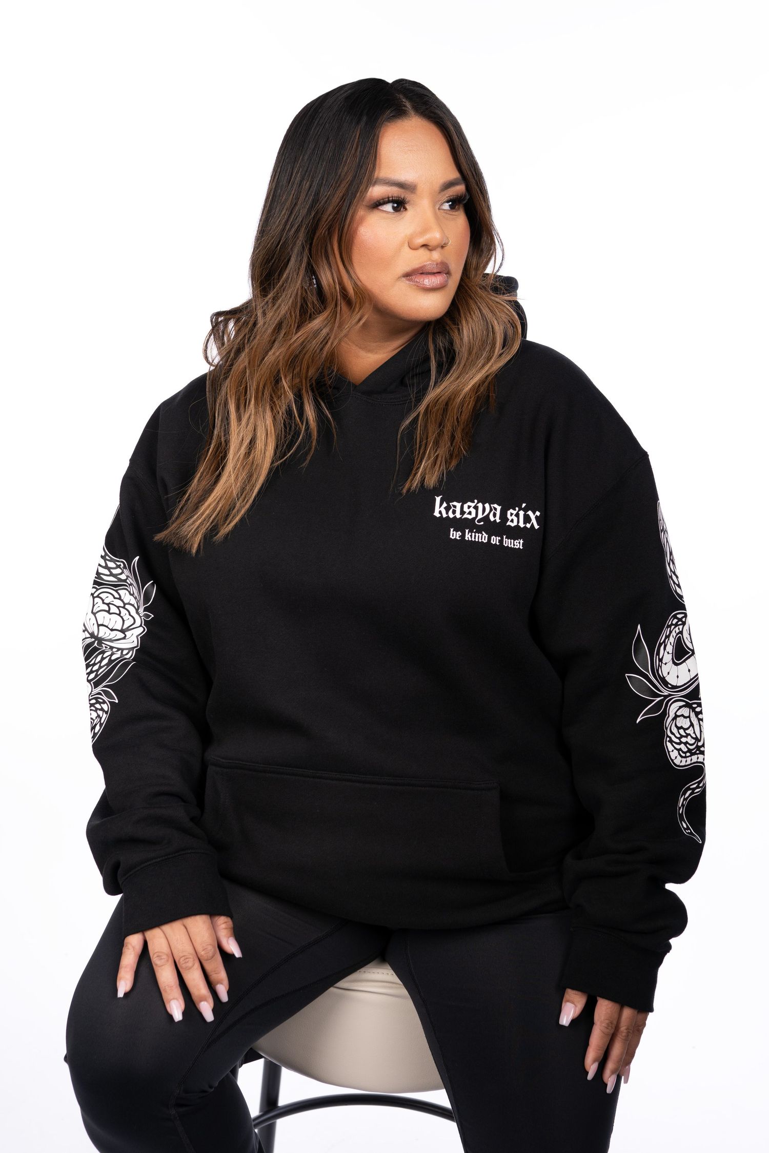 Woman wearing black oversized hoodie with floral sleeve print and 'kasya six' logo, paired with black leggings.