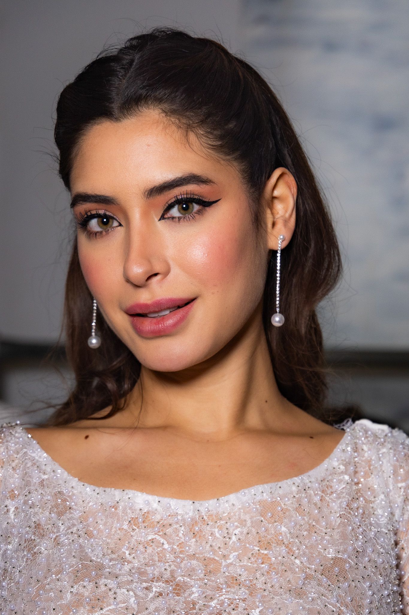 Close up portrait showing glamorous evening makeup and dangling pearl earrings with a white sequined dress.