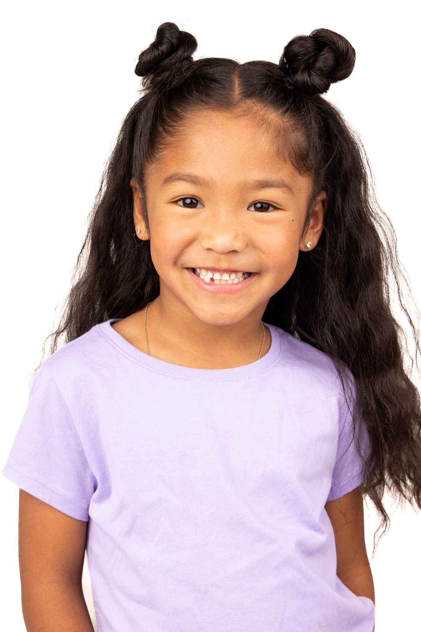 Child wearing purple shirt with dark hair styled in two buns smiles brightly at camera.