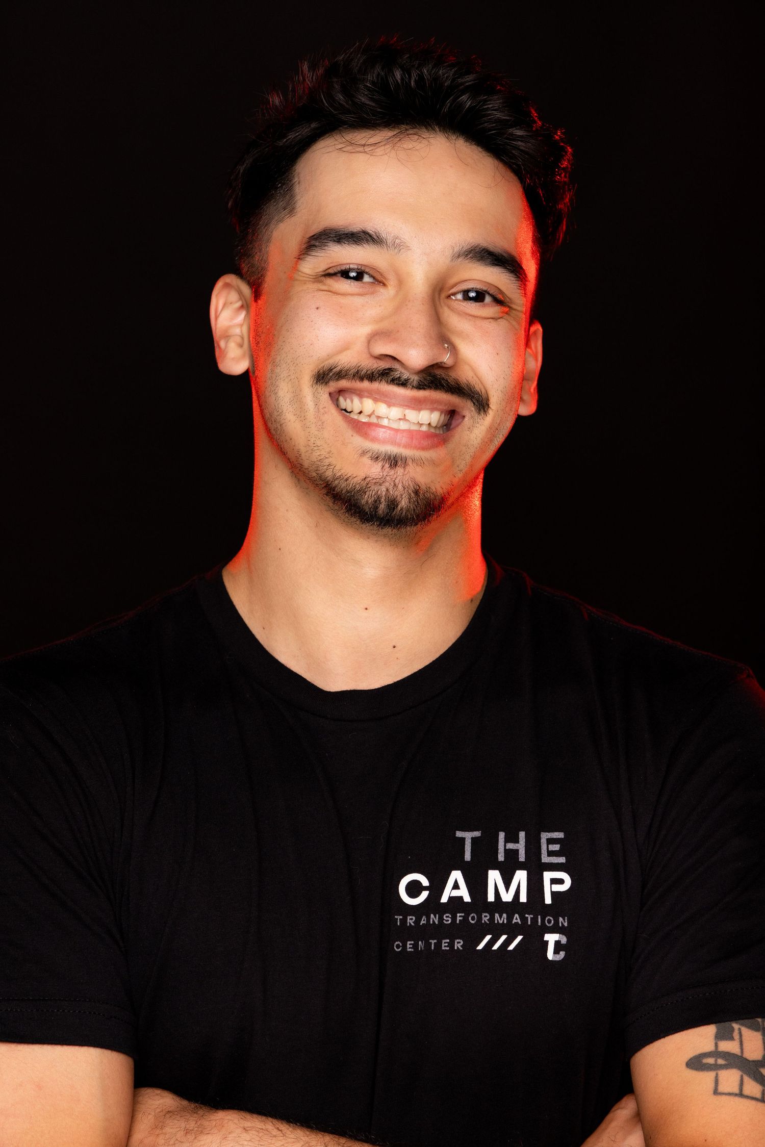 A person wearing a black t-shirt with text smiles against a dark background.