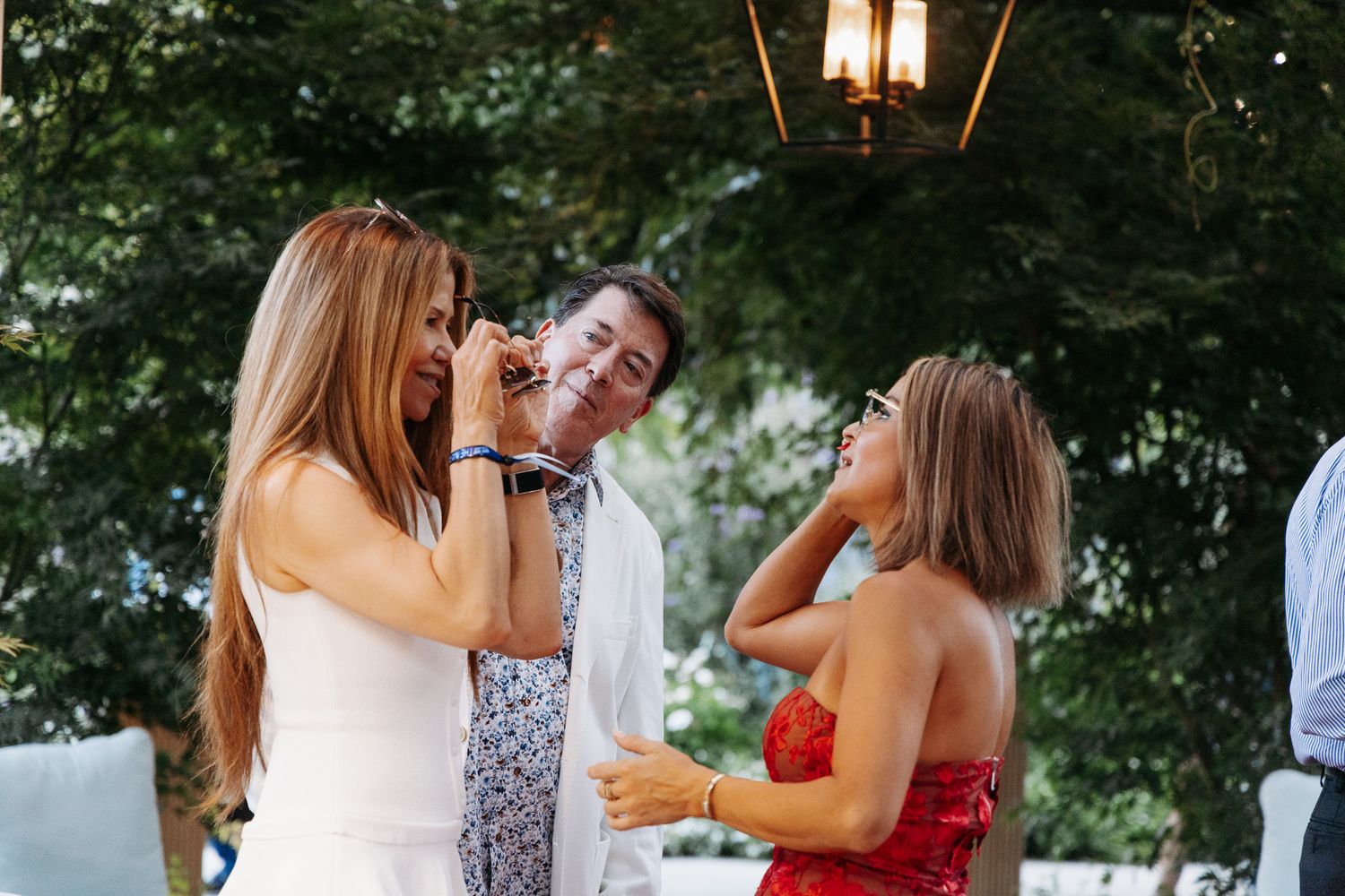 People enjoying drinks and conversation at an outdoor party under a hanging lantern light.