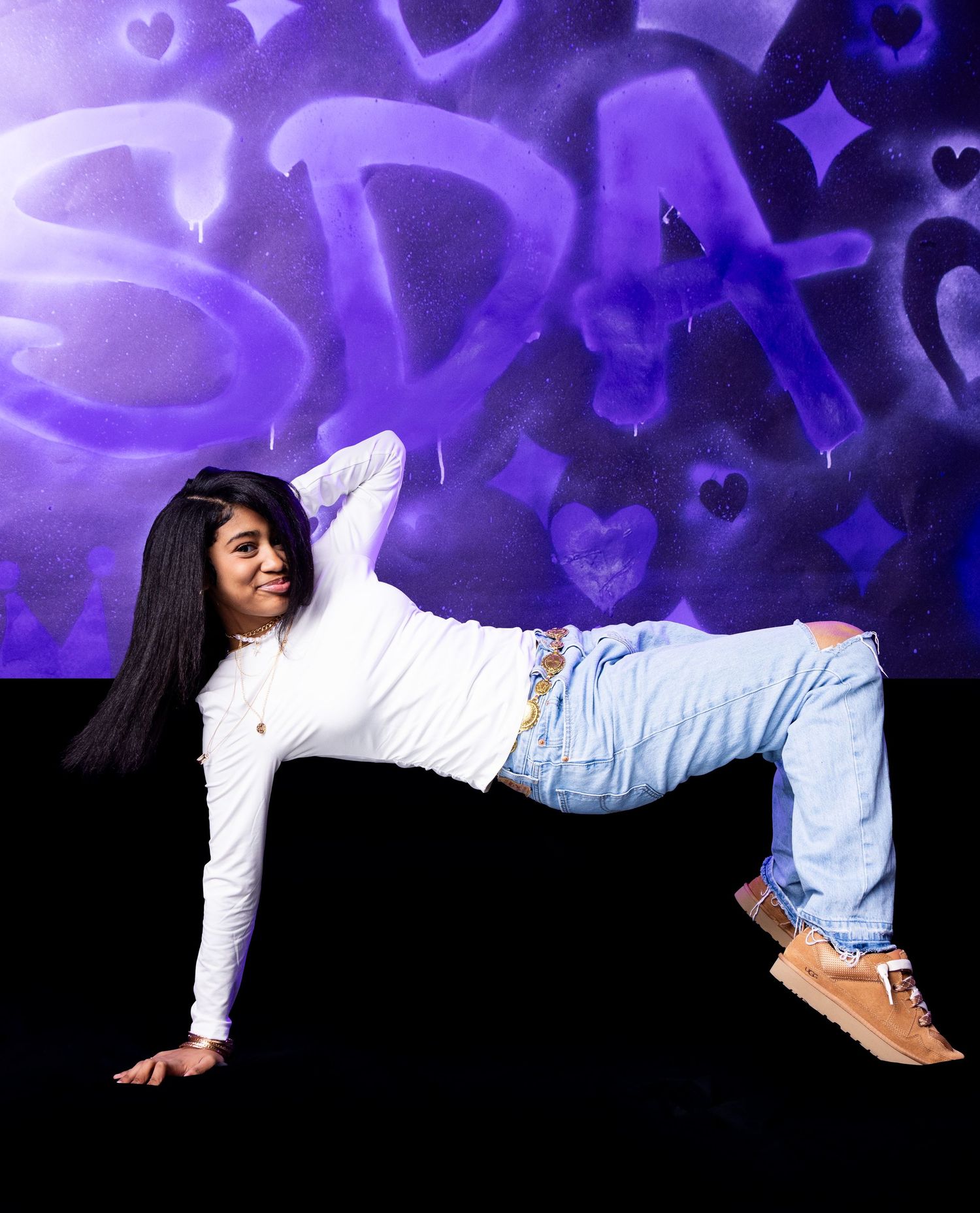 Young woman in white top and jeans poses dynamically against a purple graffiti backdrop.