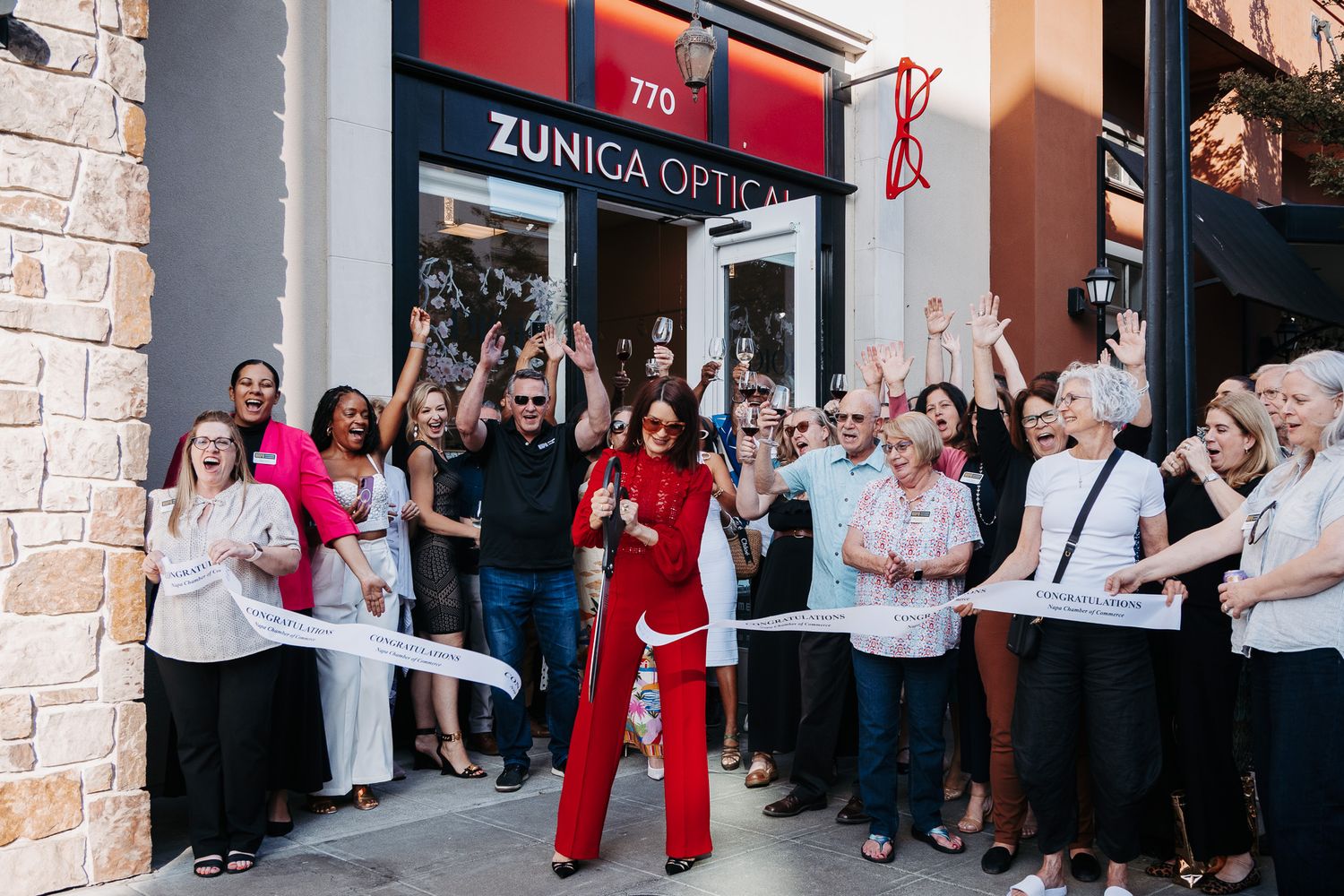 A group of people line up outside a retail storefront with red and white decor for a grand opening event.