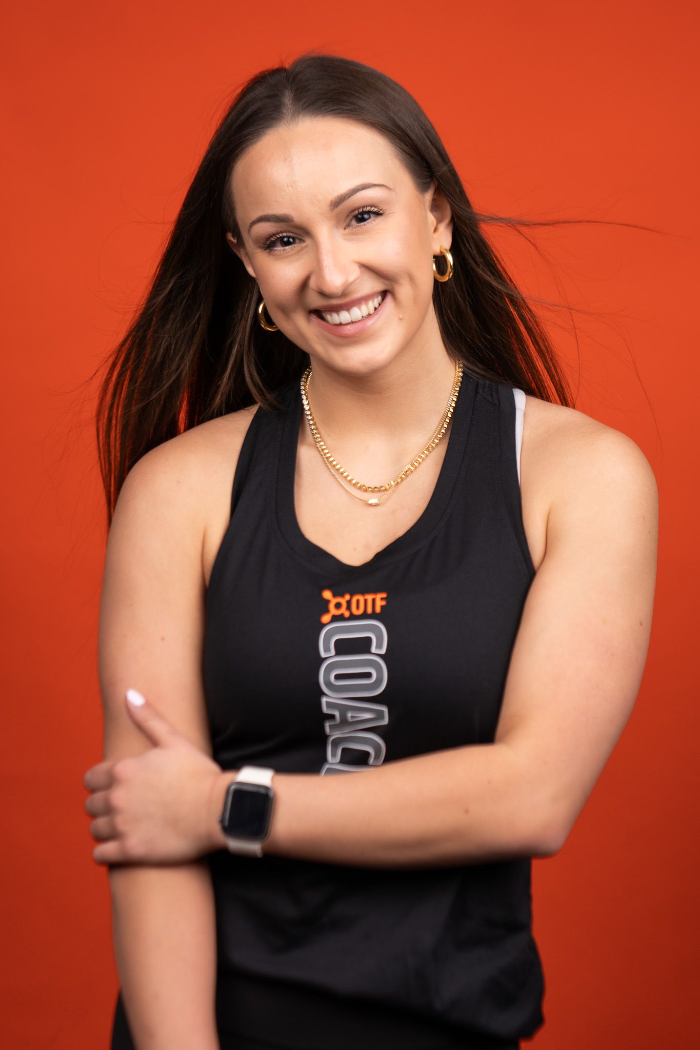 Portrait of someone in a black sleeveless jersey against a vibrant orange background with a bright smile.
