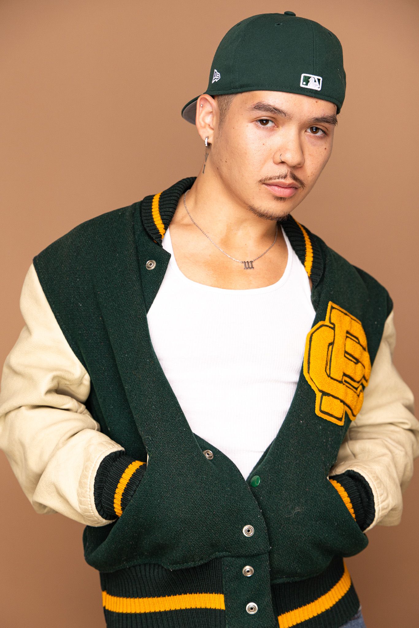 Athletic style shots in varsity jacket with green baseball cap against tan background.