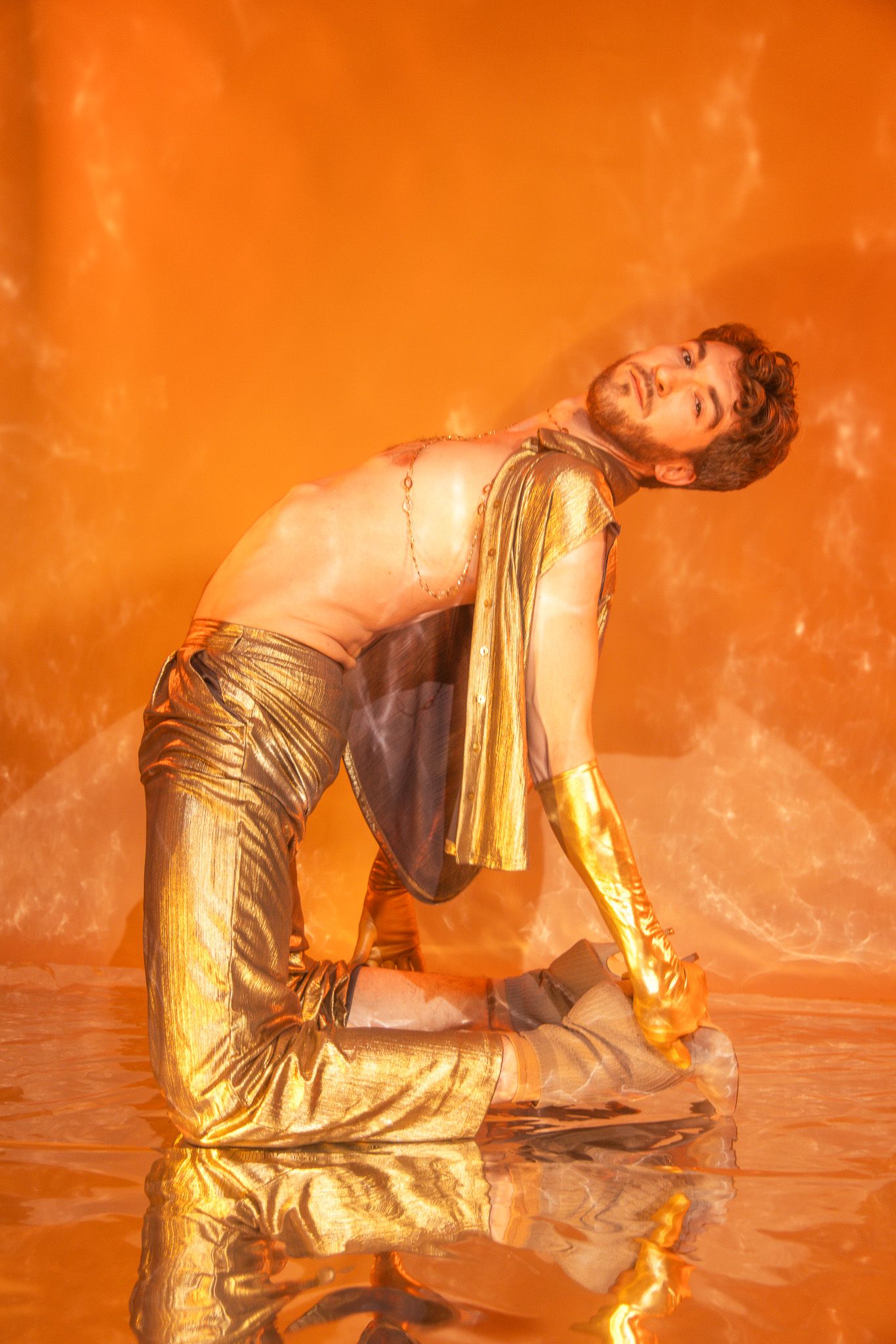 A dancer in a metallic gold bodysuit performs fluid movements against a warm orange smoky backdrop.