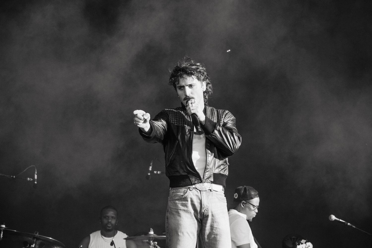 Black and white photo of a male singer performing on stage, holding a microphone and pointing at the crowd.