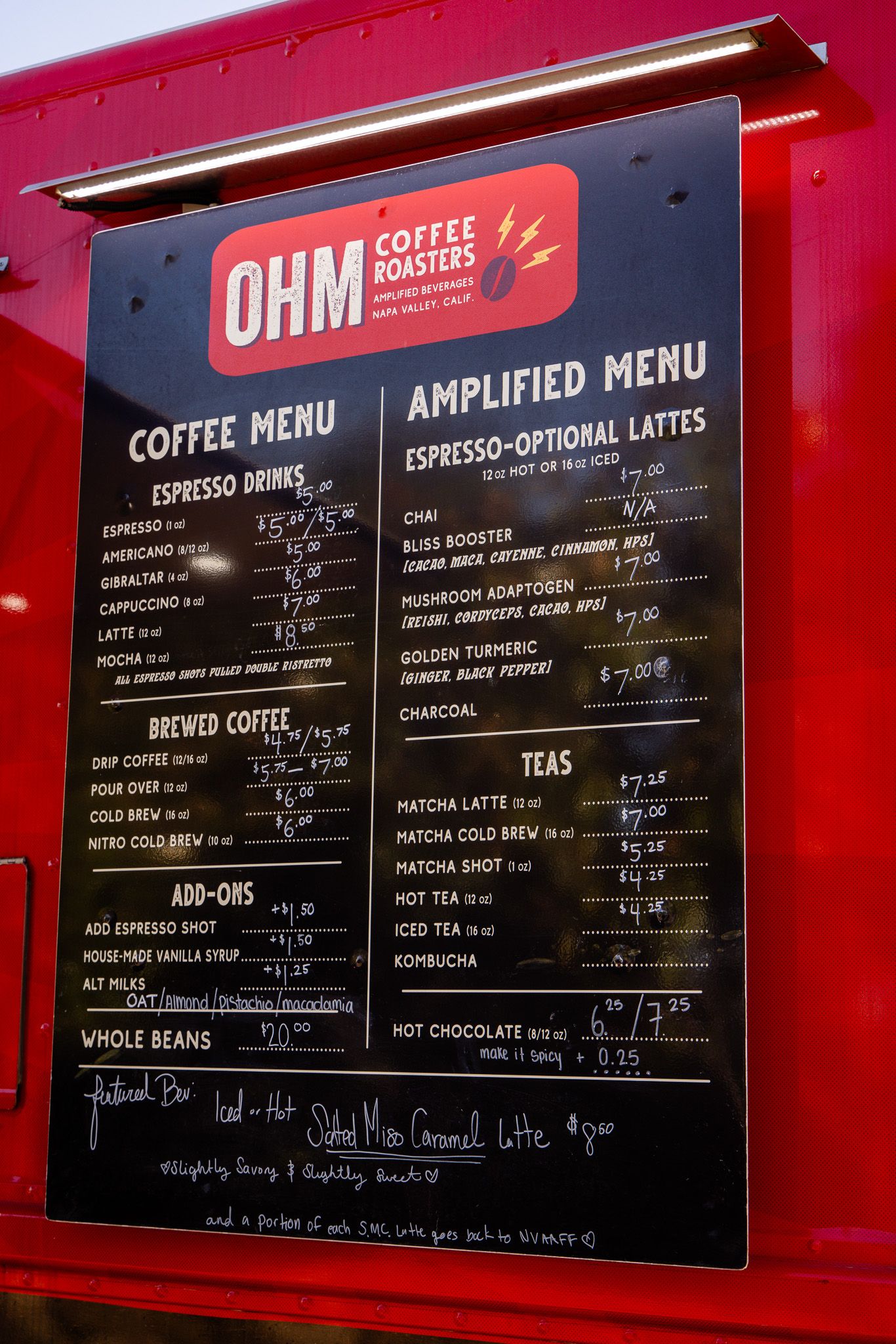 Coffee menu board for OHM Coffee Roasters displaying drink prices and specialty beverages against a red background.