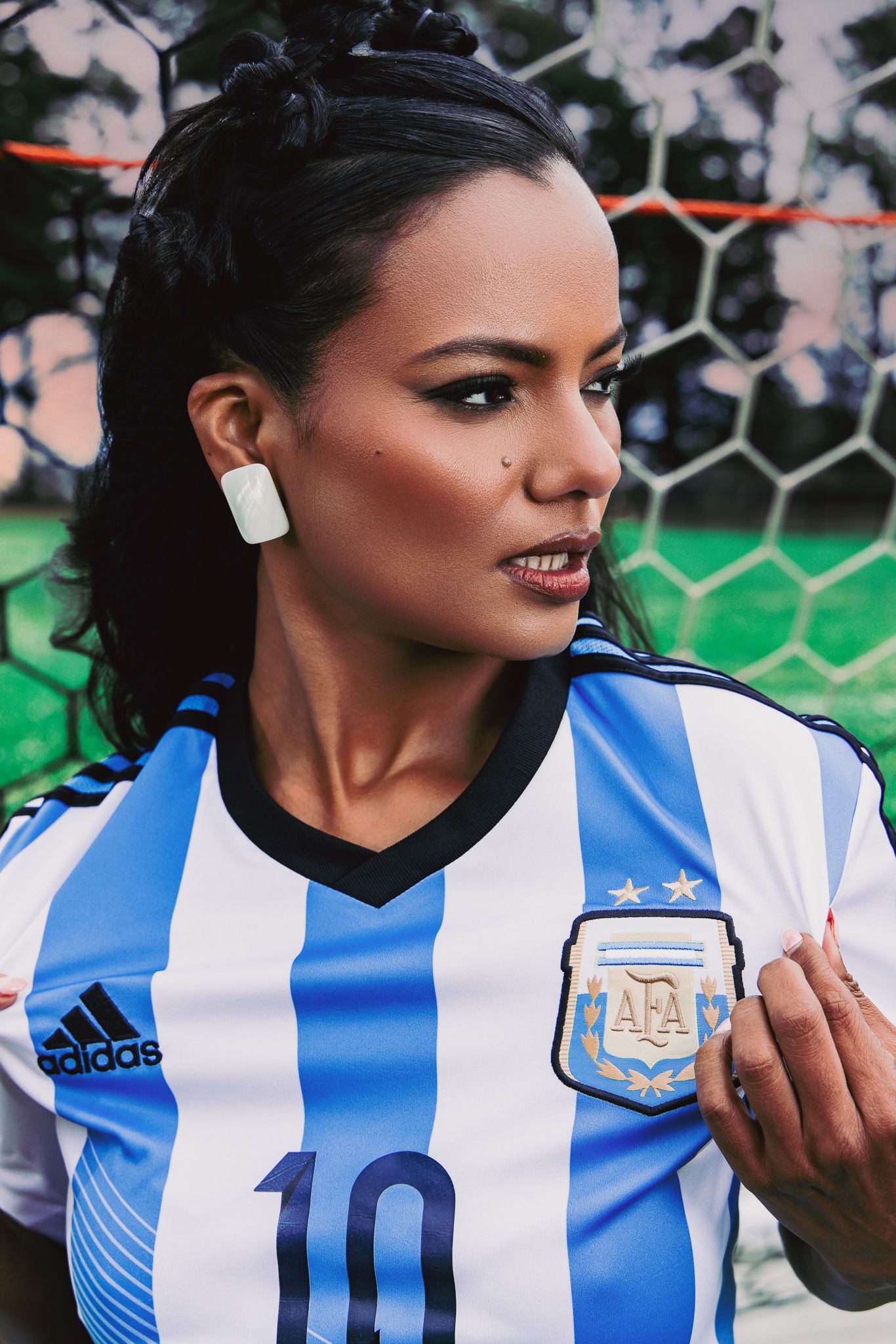 Woman wearing Argentina AFA Adidas number 10 soccer jersey posing near a football goal net outdoors.