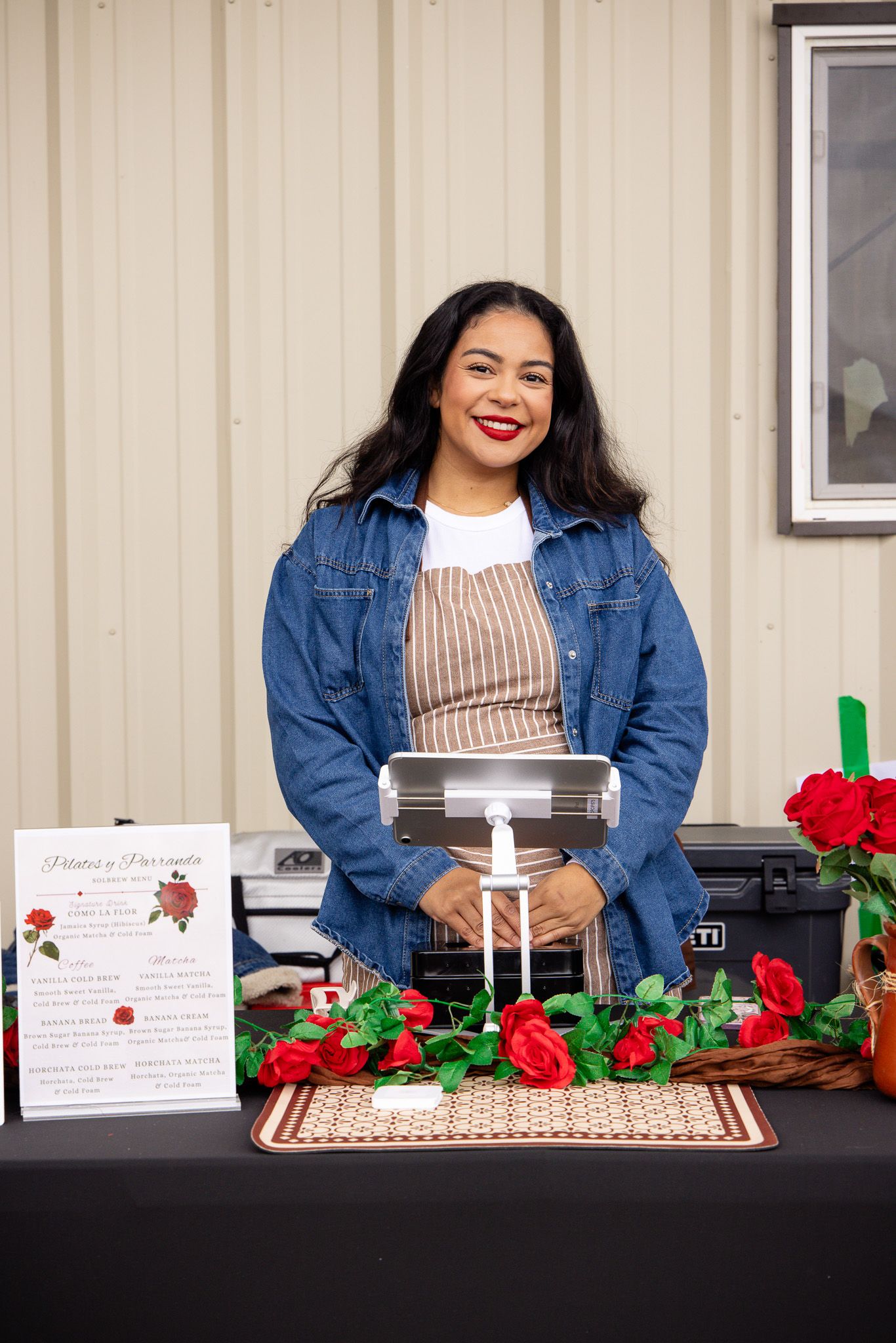 A decorated vendor table with red roses and display items against a beige wall.