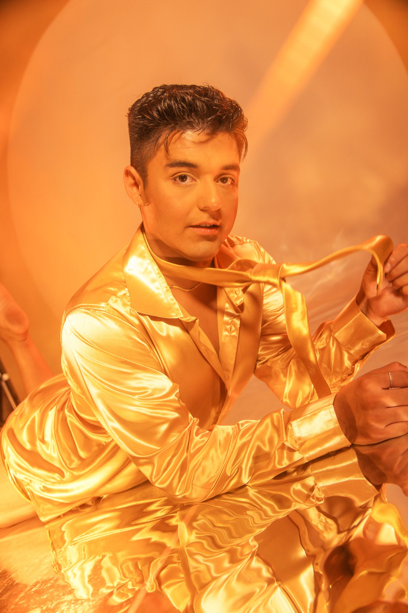 Performance artist in metallic gold outfit poses dramatically under orange lighting.