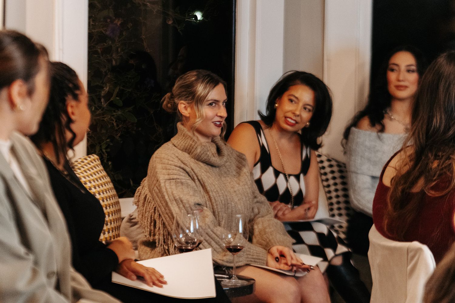 Friends socializing around a table at an indoor dinner party with dimmed ambient lighting.