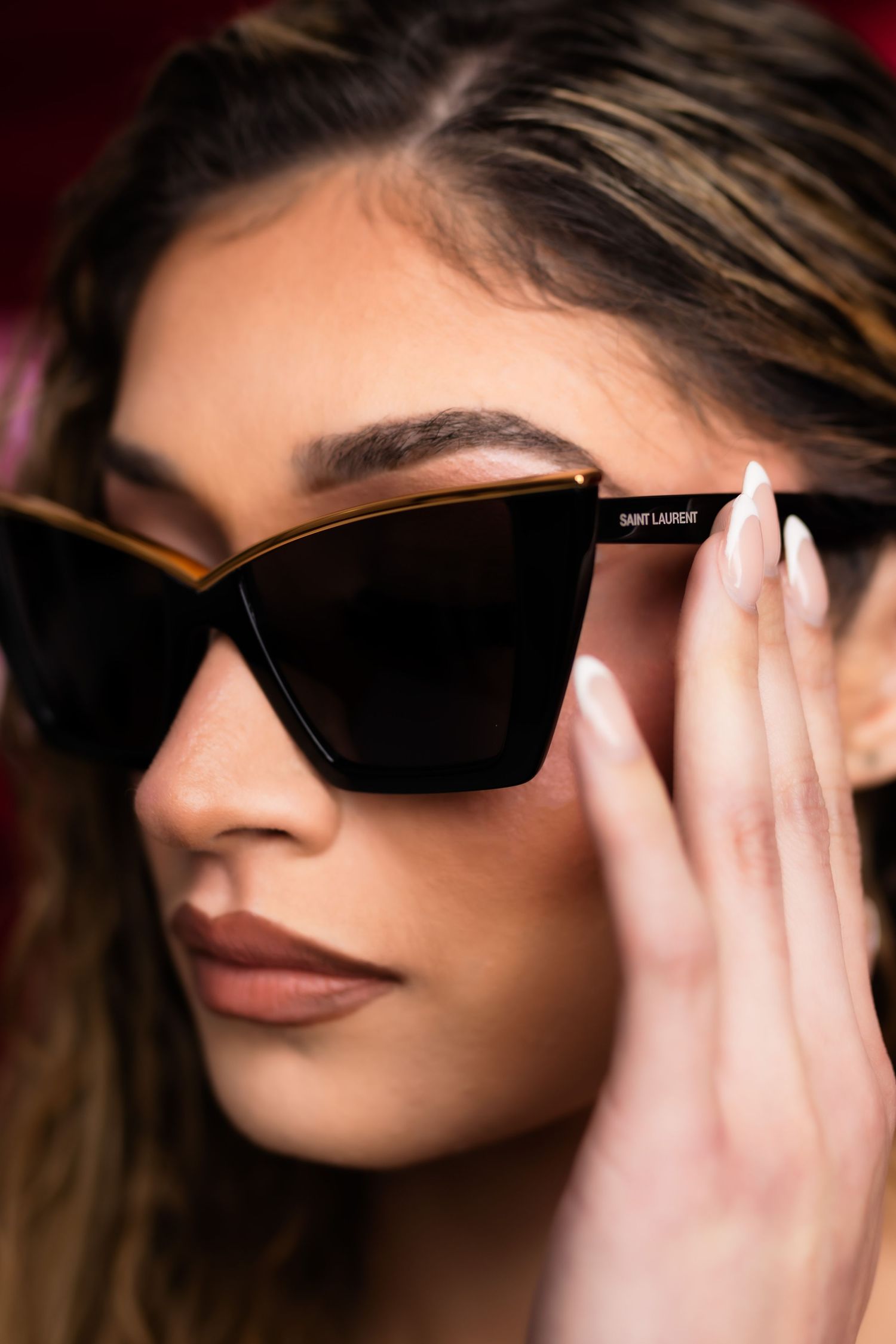 A close-up sequence showing someone adjusting black sunglasses against a dark red background.