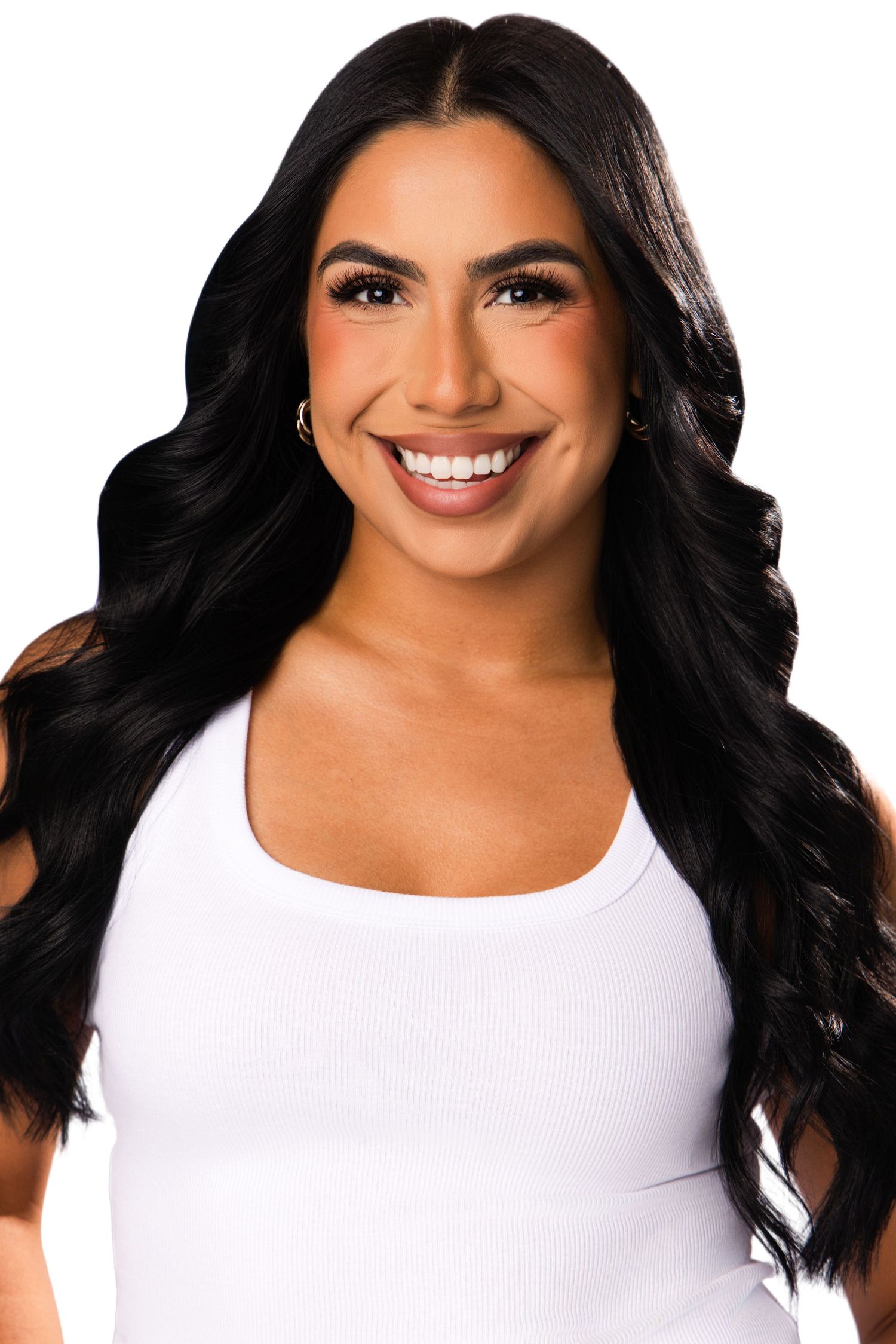 Smiling young woman with long black wavy hair wearing a white ribbed tank top against a white background.