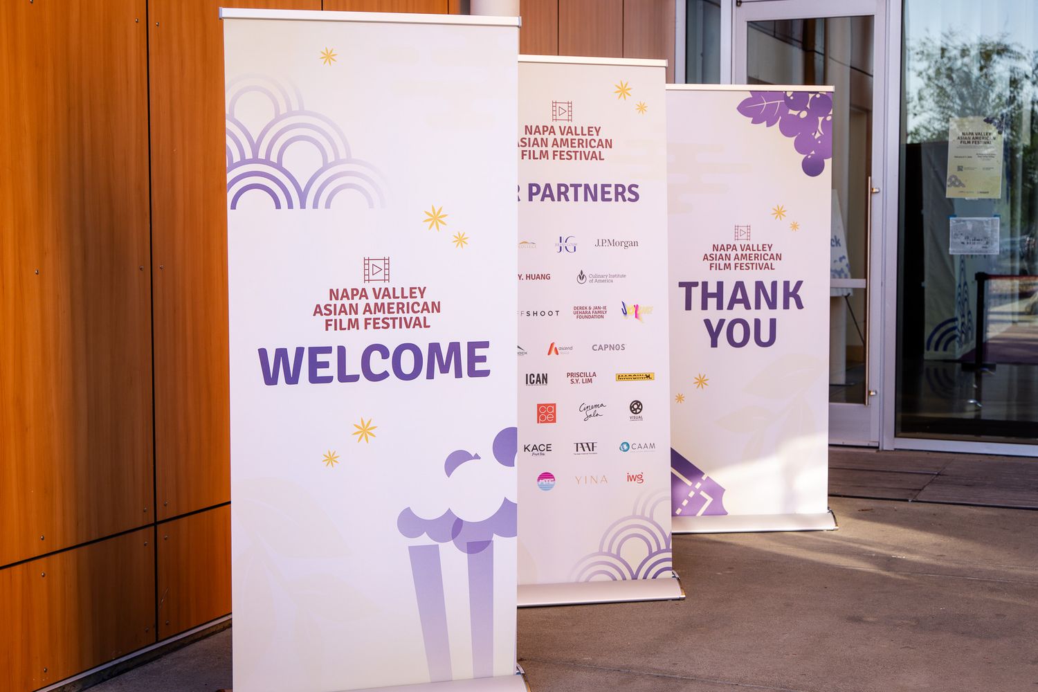 Event welcome banners with purple designs and sponsor logos displayed at a conference entrance.