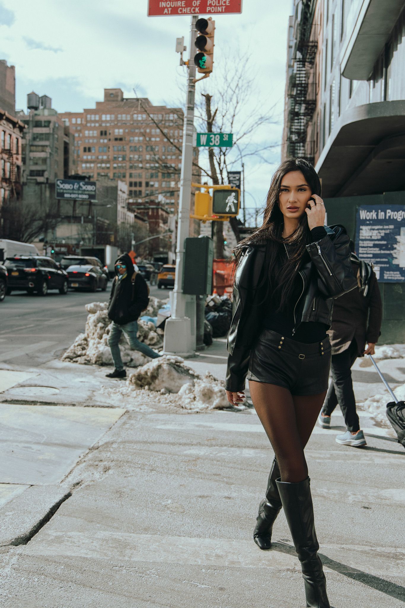 Person in black winter outfit walking on snowy city sidewalk in an urban environment during winter.