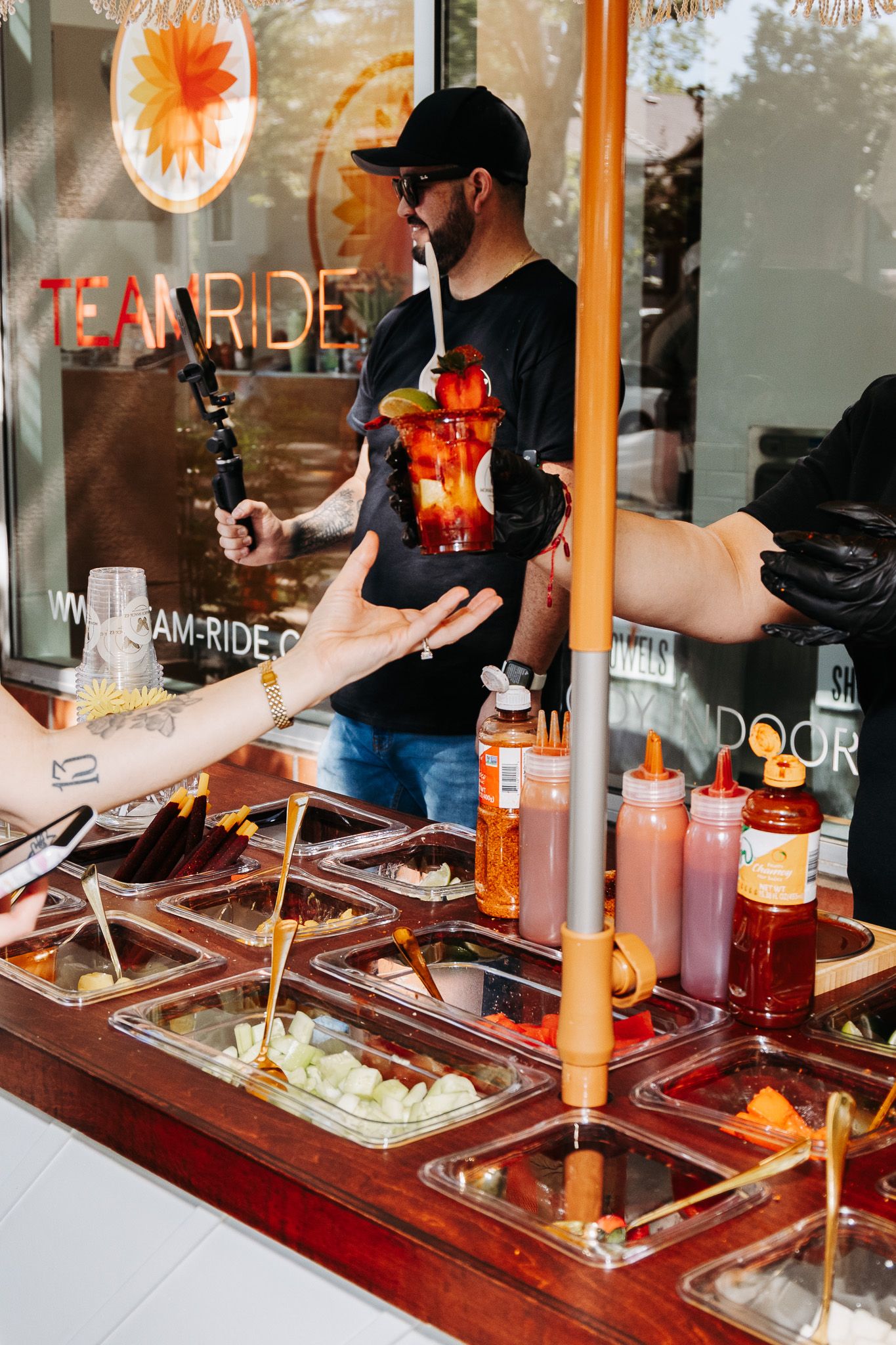 A food service worker serves customers at a buffet station with various sauces and condiments displayed in metal containers.